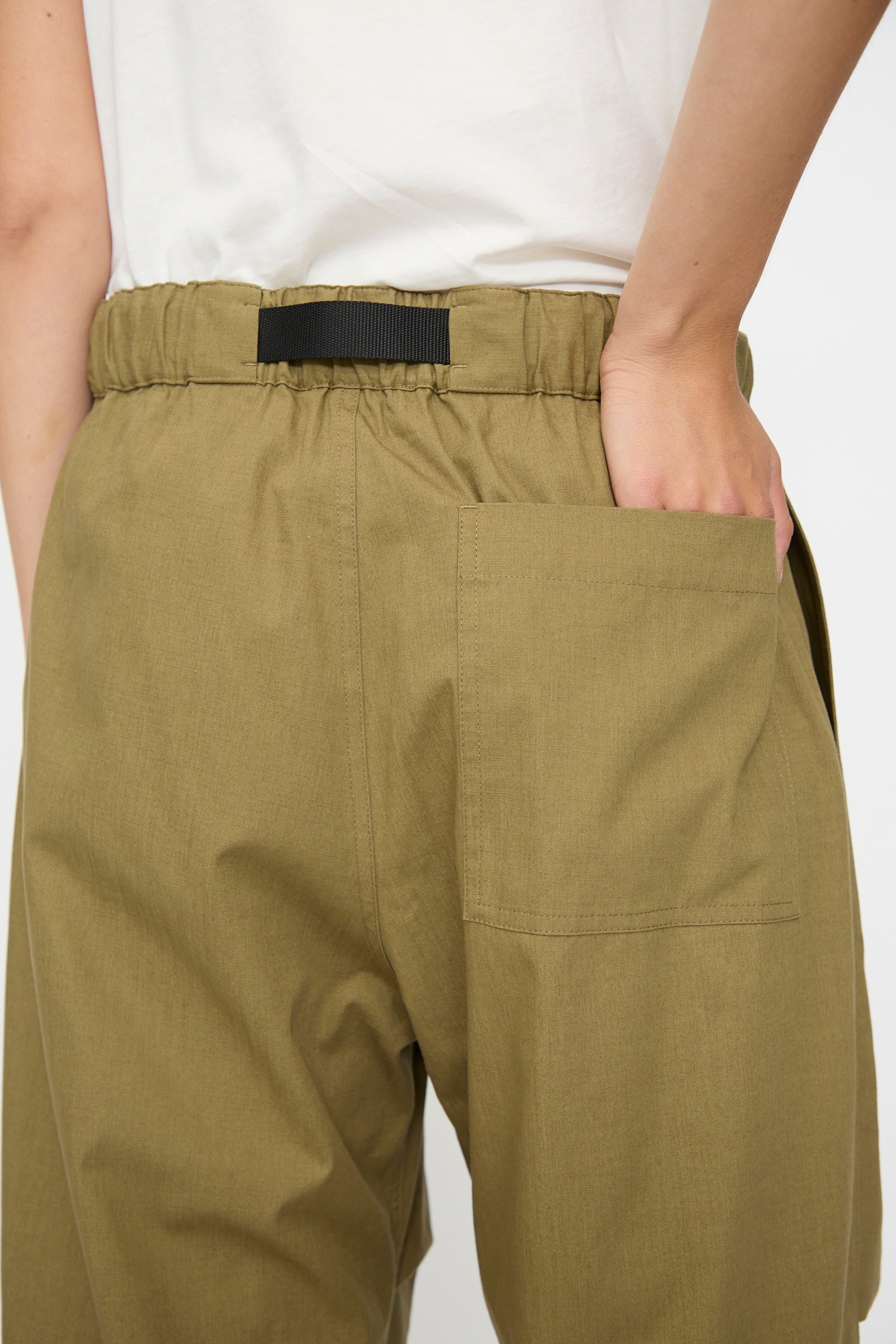 Model wearing Studio Nicholson's Caro Belted Pant in Military Green, featuring a loose fit, elastic waistband, and black buckle belt, with hand tucked in the back pocket and shown from behind.