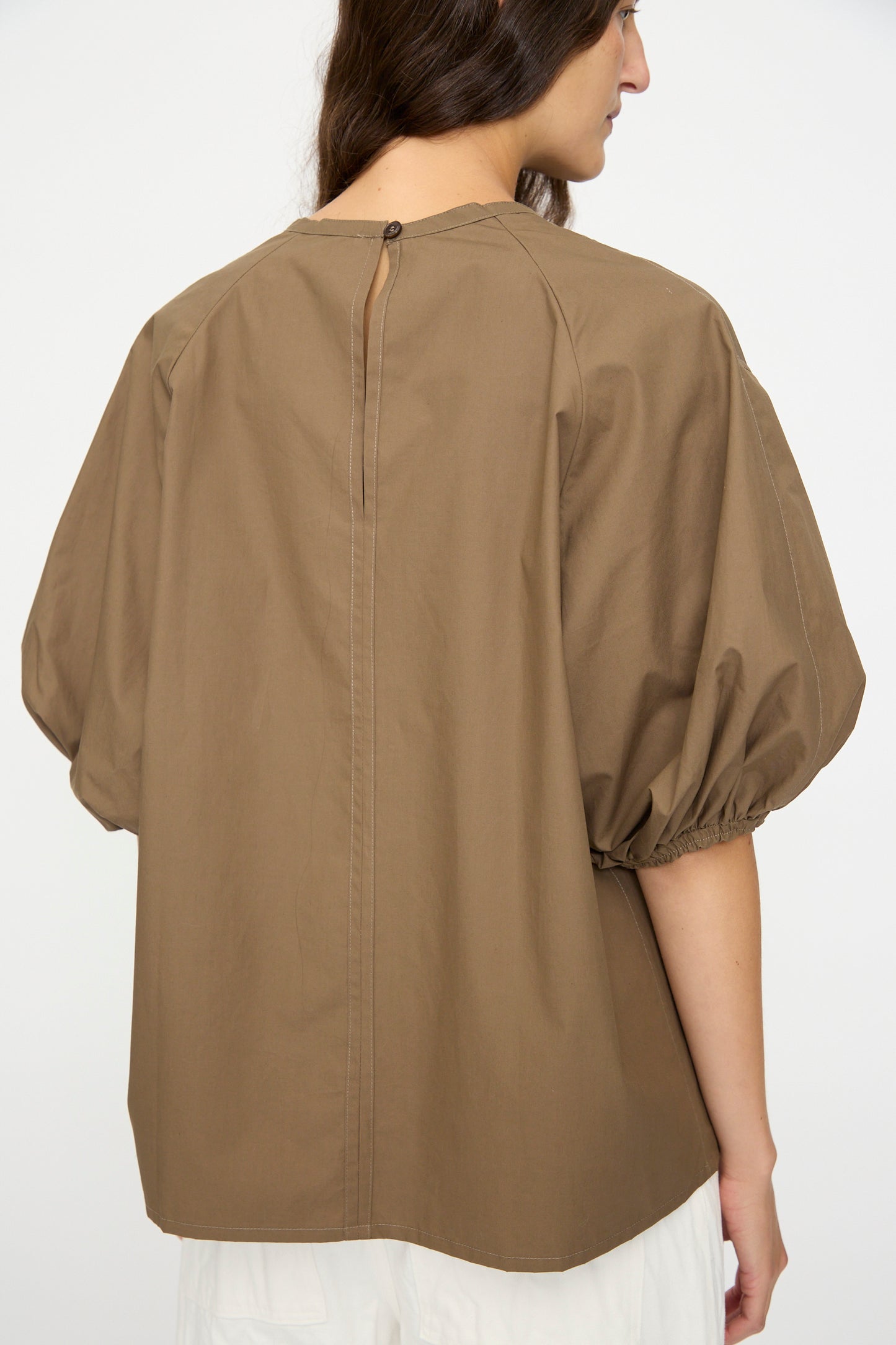 A woman wearing the Studio Nicholson Cove Gathered Top in Boulder, a relaxed-fit brown cotton short sleeve.