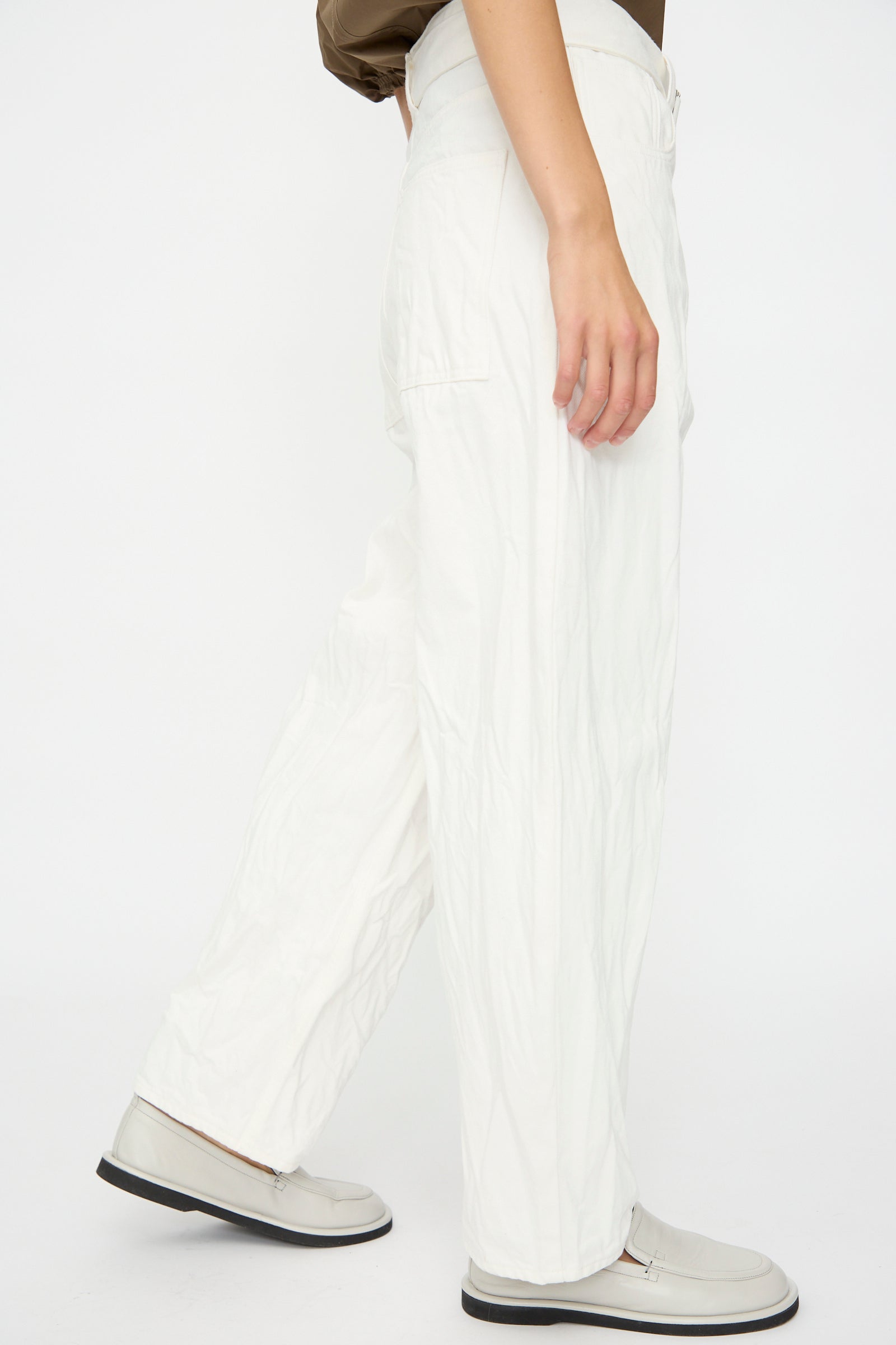 A person wears Studio Nicholson’s Denim Cahun Skater Pant in White and light shoes, standing against a plain white background.