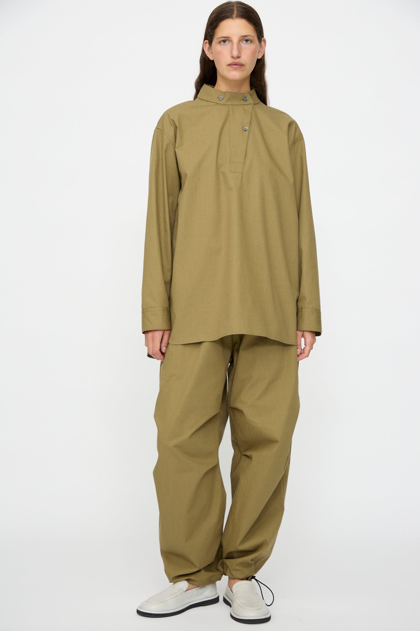 A person wears the Studio Nicholson Dimas Grandad Collar Shirt in Militaire with matching wide-leg khaki pants and white shoes, standing against a plain white background.
