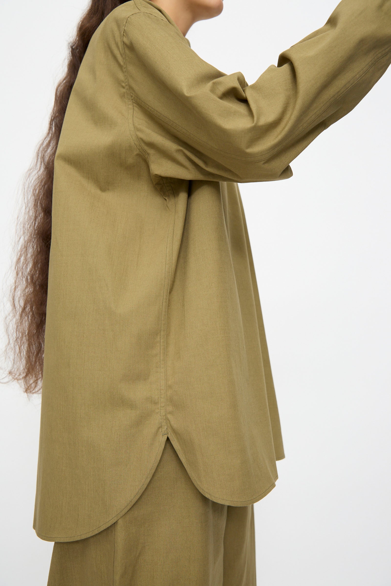 Person with long, wavy brown hair wearing Studio Nicholson's Dimas Grandad Collar Shirt in Militaire, shown from the side against a plain background.