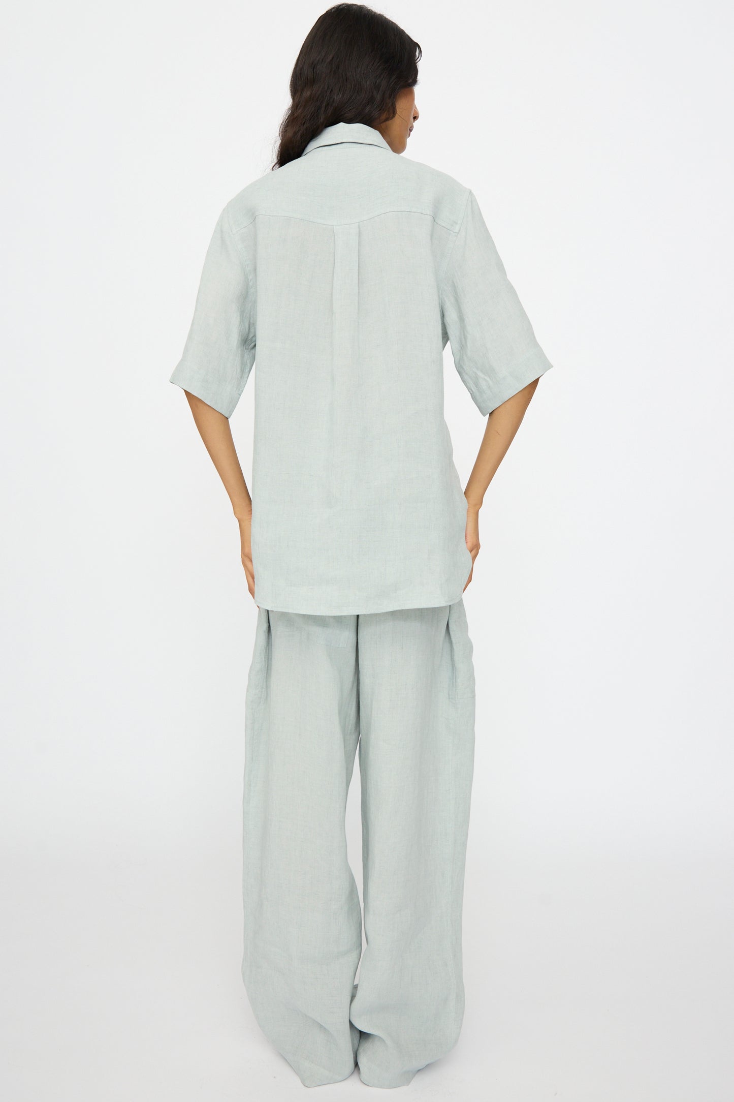 A person stands with their back to the camera, wearing the Studio Nicholson Estes Shirt in Spearmint, styled in a relaxed fit, against a plain white background.
