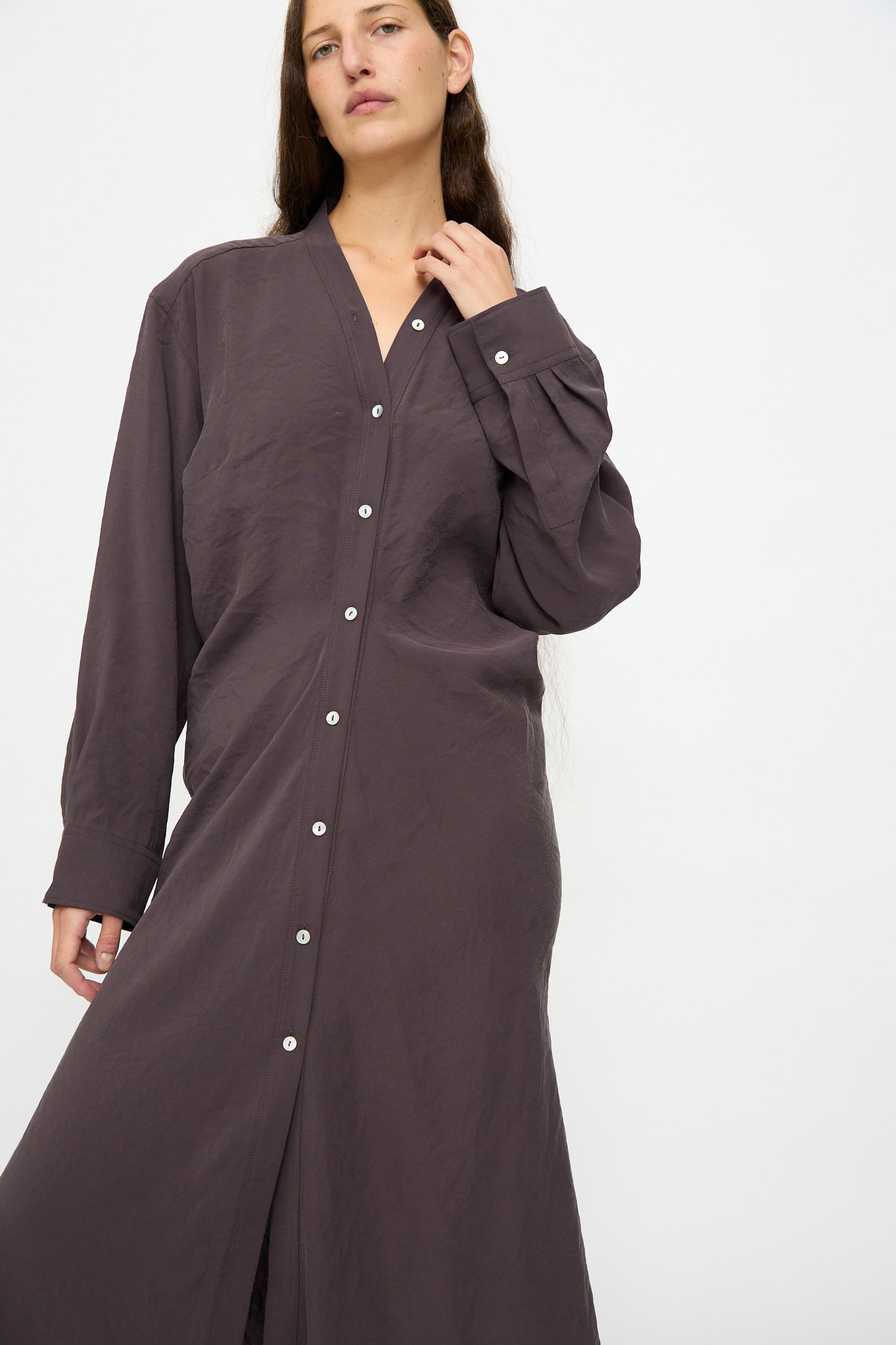 A person wears the Studio Nicholson Fiore Shirt Dress in Yam, a loose-fitting, long sleeve button-down made from Italian-milled modal, standing against a plain white background.