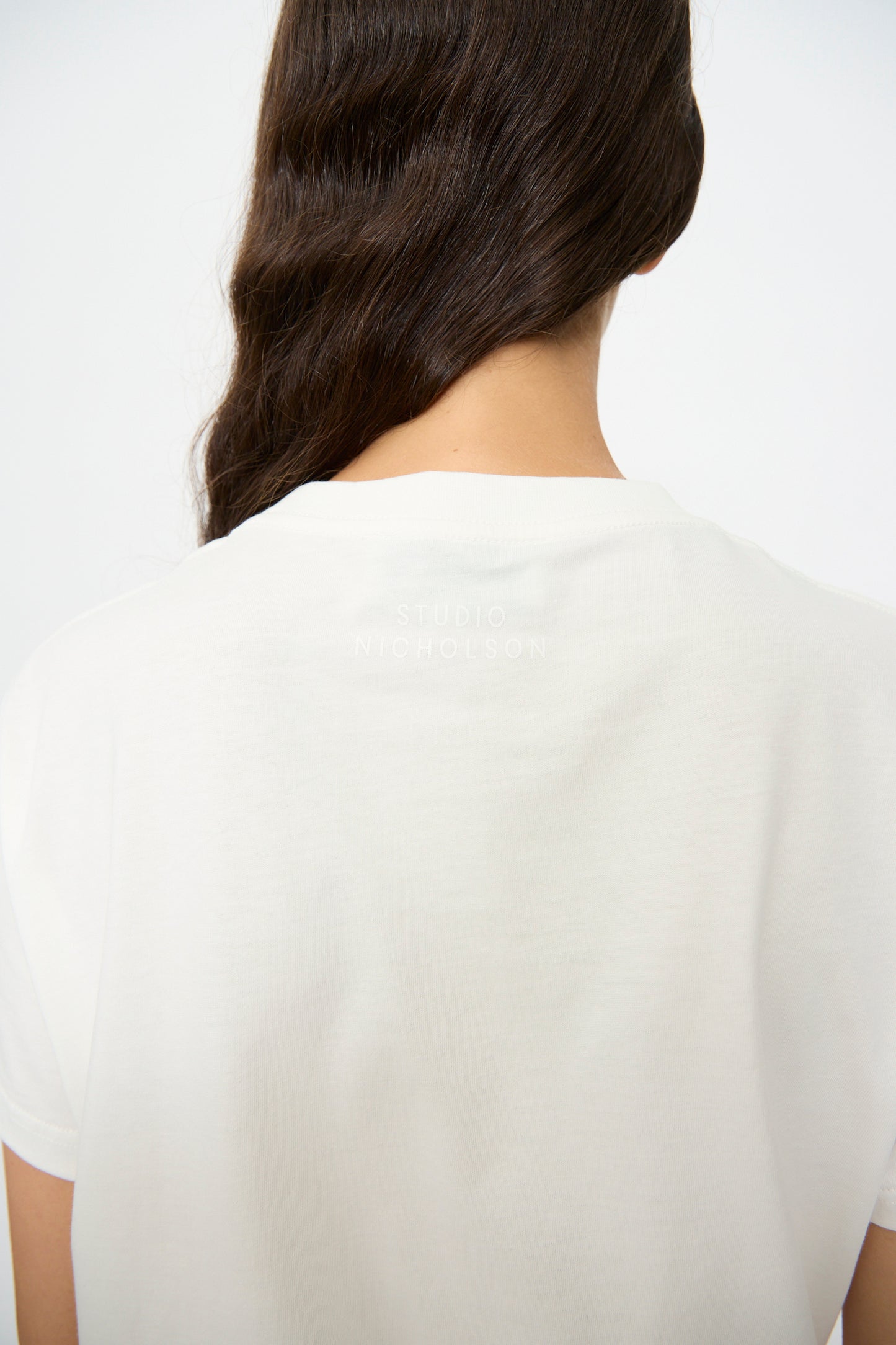 The back view of a person wearing the Studio Nicholson Marine Perfect Tee in Off White, featuring subtle "STUDIO NICHOLSON" branding on the upper back.