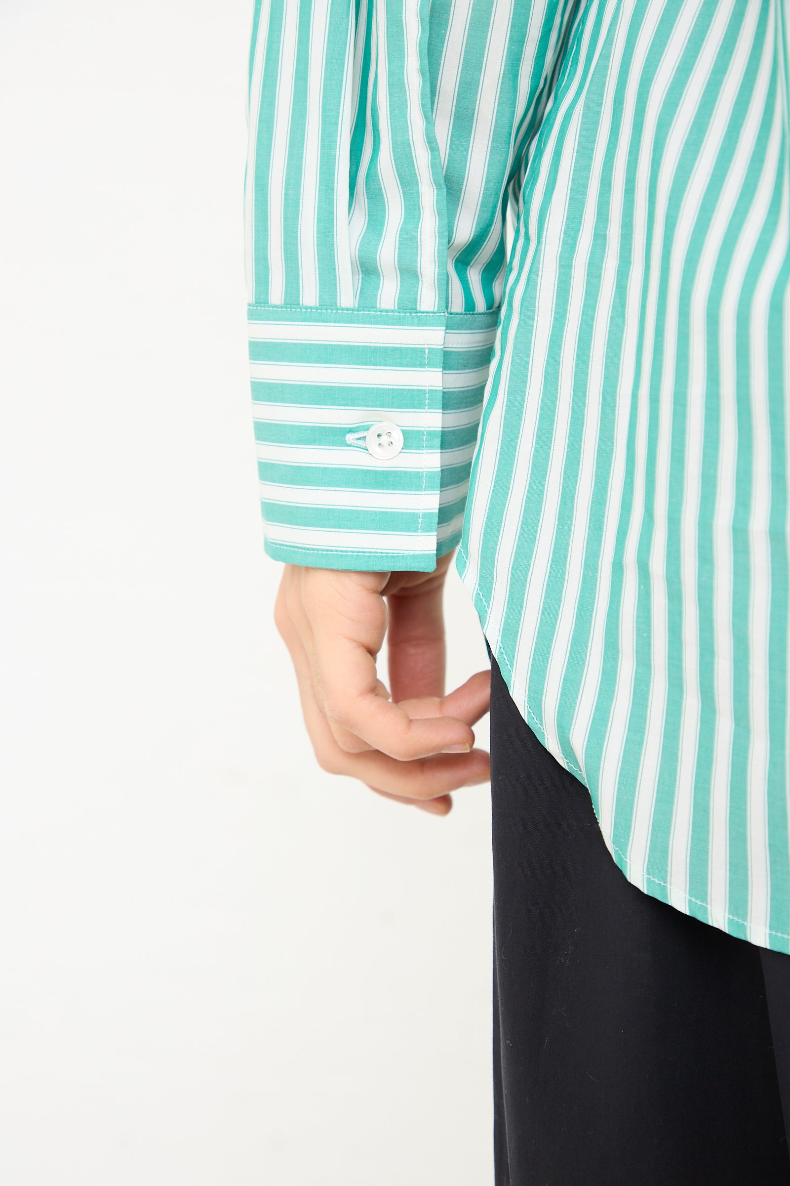 A close-up of a person wearing a Studio Nicholson Santos Overshirt in Green and Cream with a buttoned cuff.