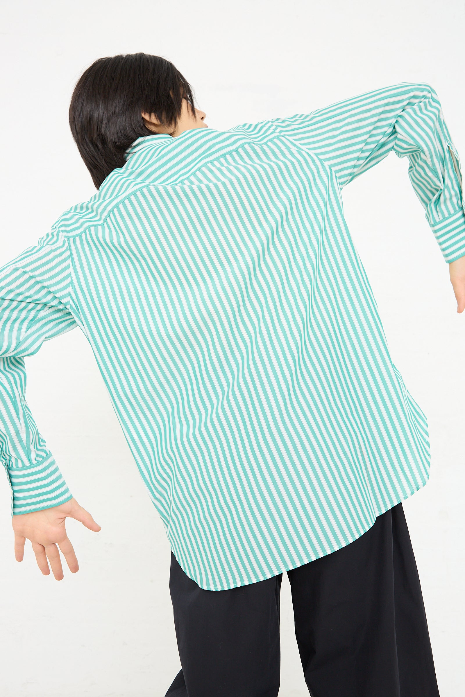 A person facing away from the camera wearing a Santos Overshirt in Green and Cream by Studio Nicholson and black trousers.