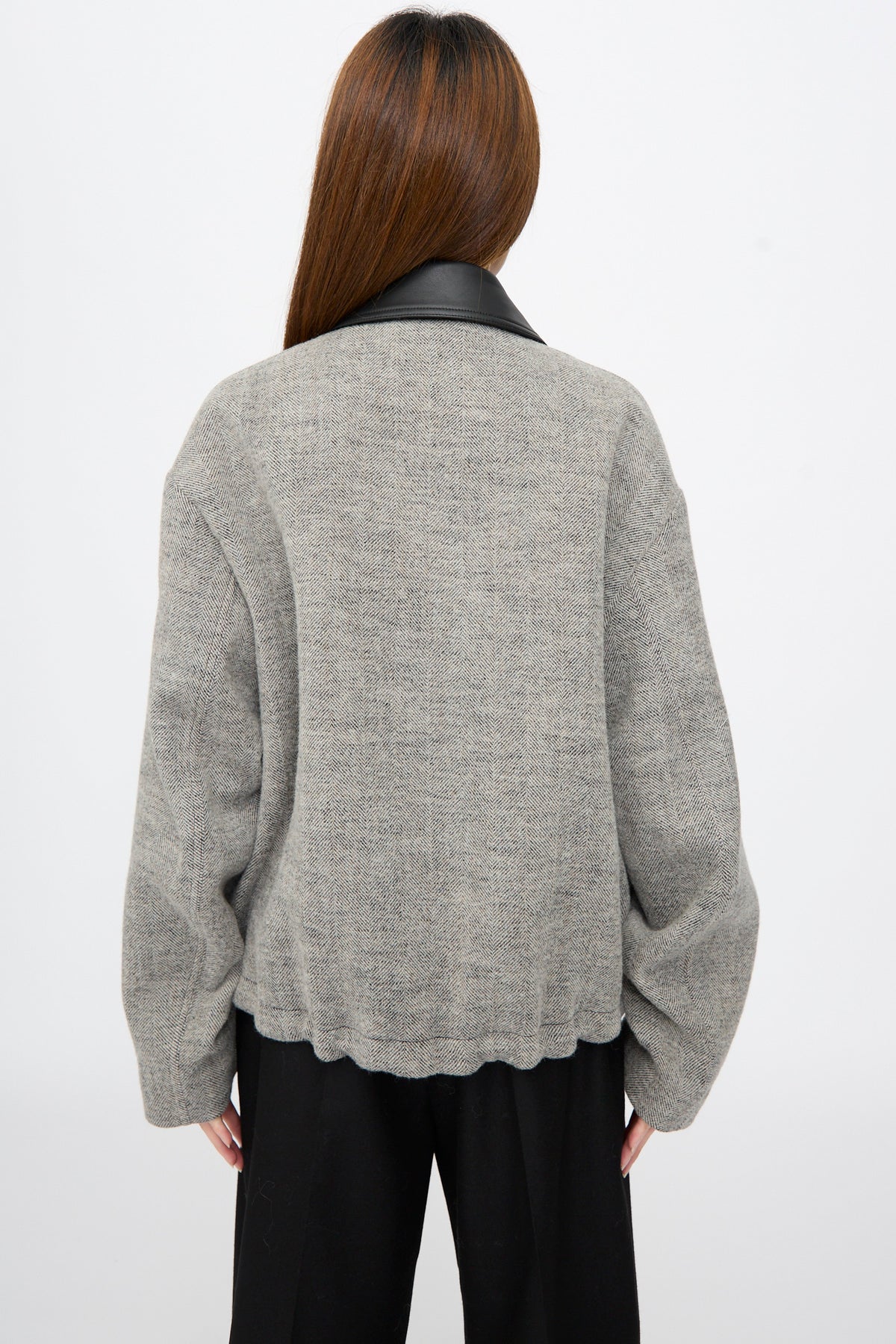 Back view of a person wearing a textured, gray herringbone Seberg Chore Jacket in Black and White with a black collar over black trousers.