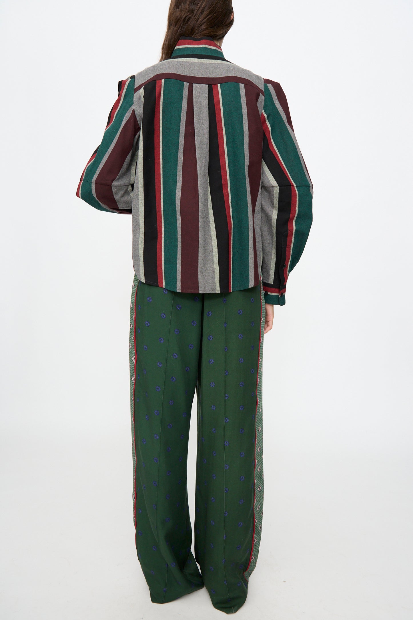 A person stands with their back to the camera, wearing the TOGA ARCHIVES Flannel Striped Shirt in Green—crafted in Japan—and loose green pants with a subtle pattern, against a plain white background.