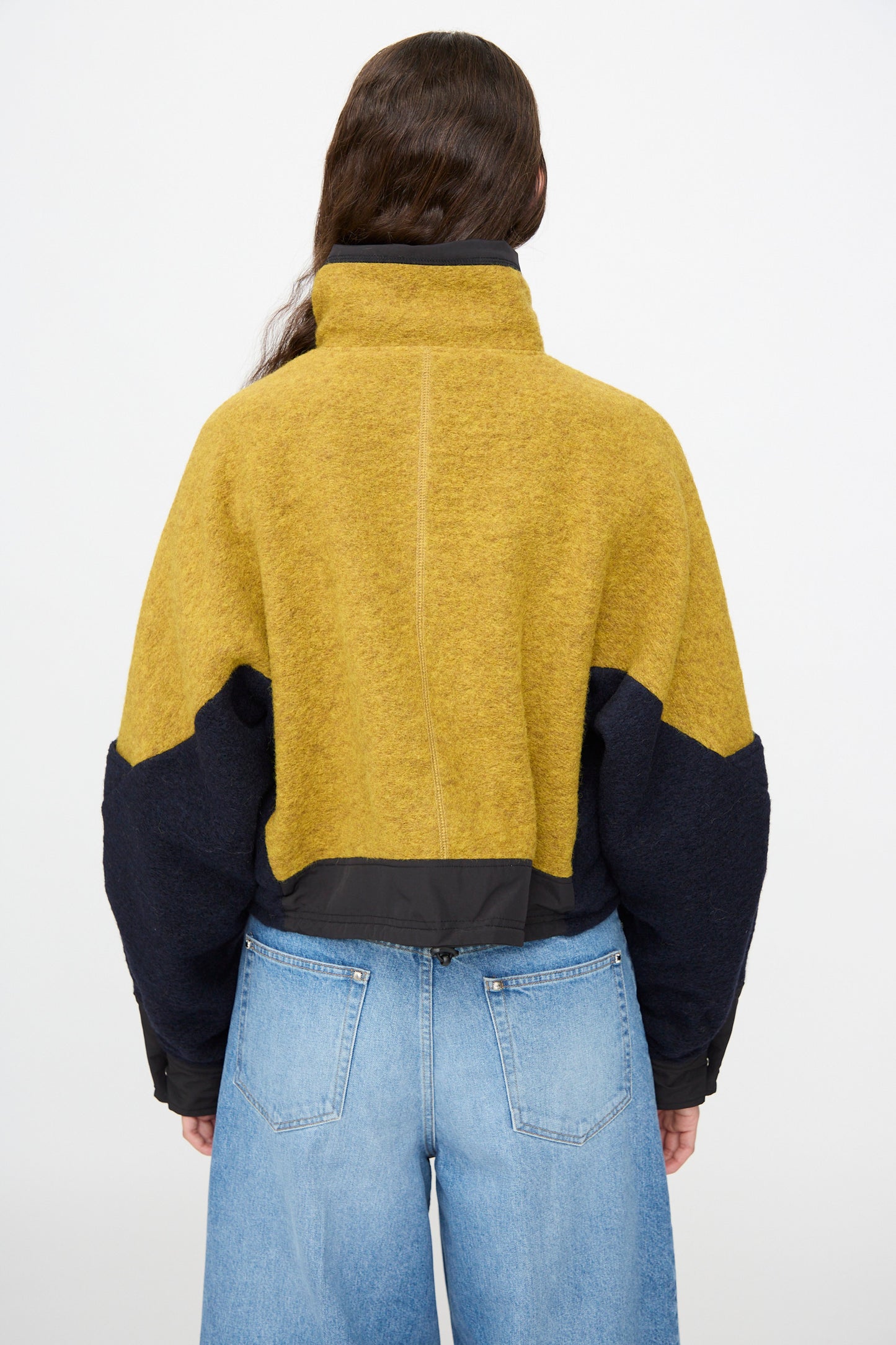 A person with long brown hair, seen from the back against a plain background, is wearing the TOGA ARCHIVES Wool Jersey Blouson in Navy and light blue jeans.