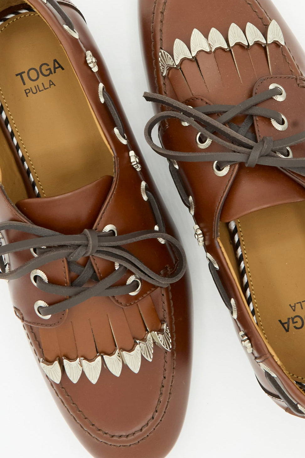 Close-up of the TOGA ARCHIVES Leather Flat in Brown, featuring gray laces, fringe detailing, and silver decorative accents on the top and sides.