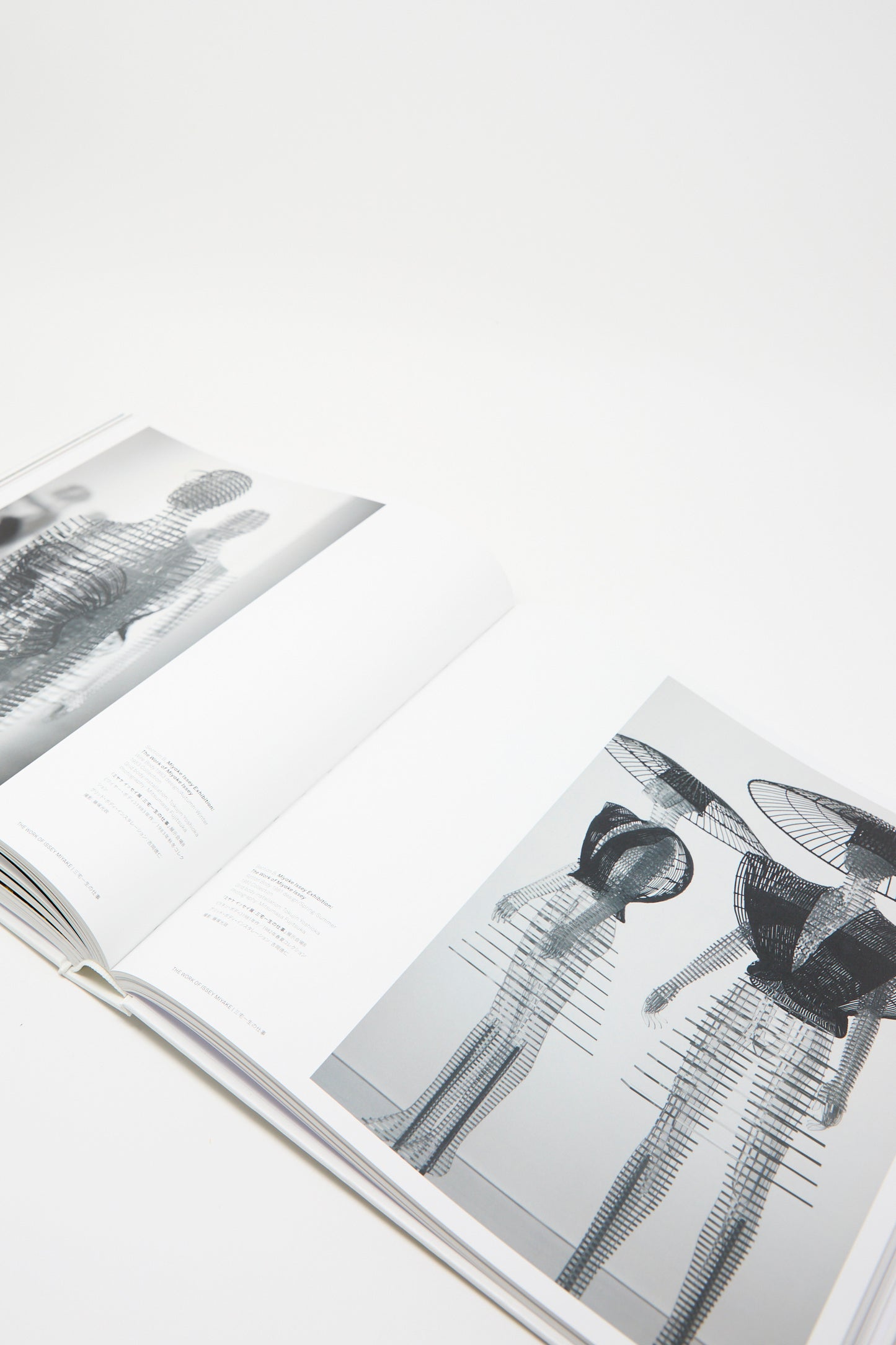 An opened page of the book, produced by Taschen, displays black and white abstract sculptures on its pages, encapsulating the vision of Issey Miyake. Photographed against a black background.