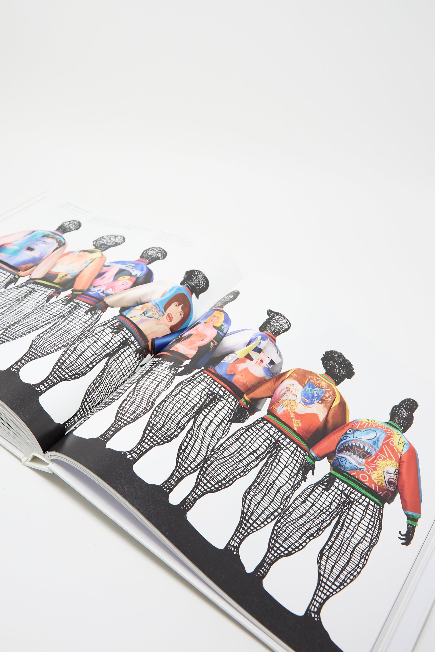 The open page of Taschen's book showcases a series of figures, each dressed in vibrant, artistic designs that reflect Issey Miyake's vision. Set against a white background.