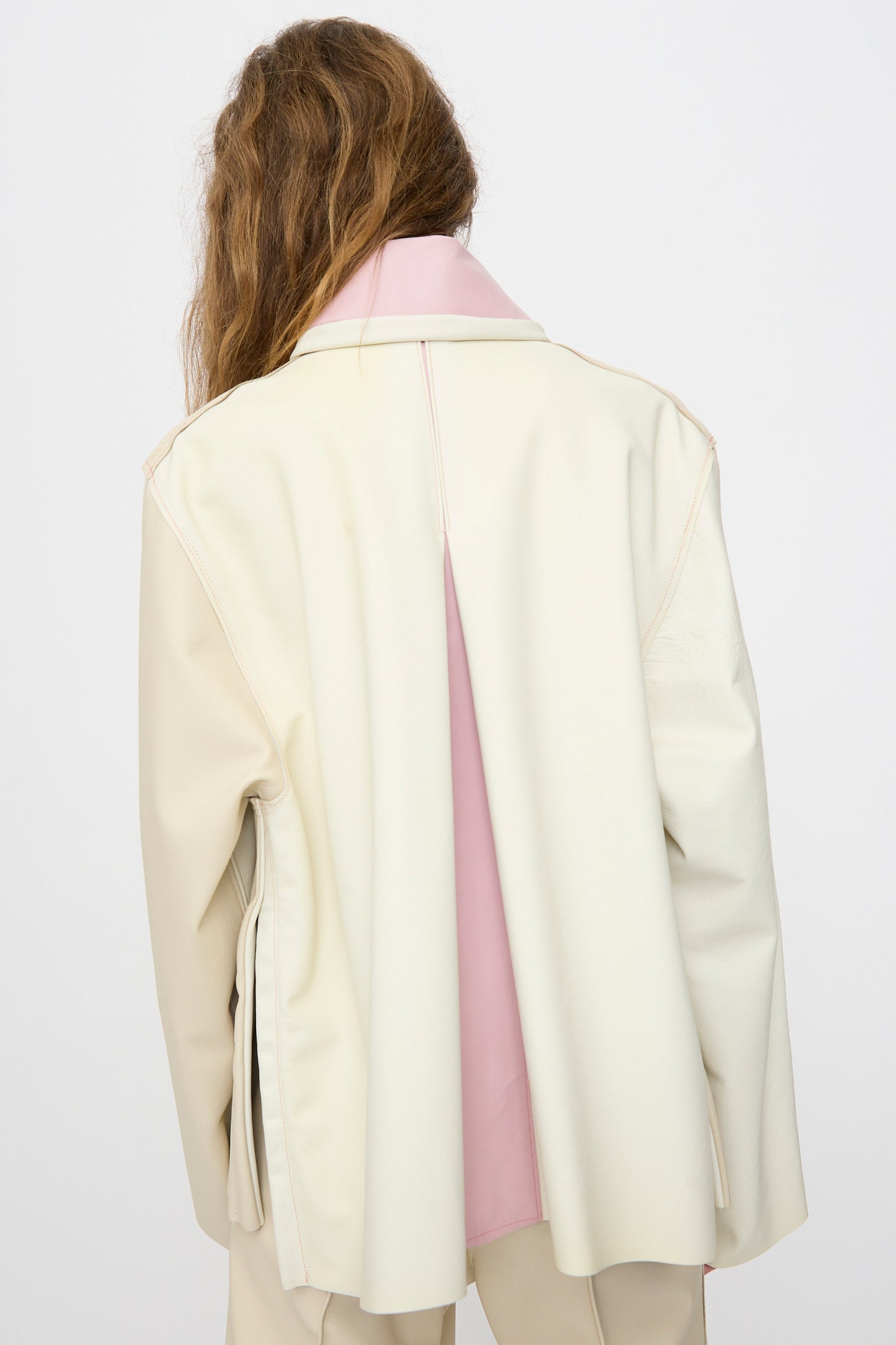 A person with long brown hair is shown from the back wearing the Thank You Have A Good Day Leather Chore Jacket in Ecru, featuring a pink inner lining, against a plain white background.