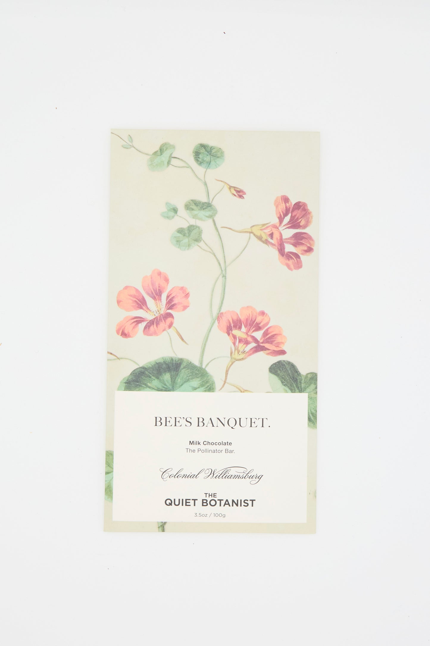 The beige packaging of The Quiet Botanist's Bee's Banquet Bar features a botanical design with pink flowers and green leaves, labeled as "Milk Chocolate" with Bee Pollen, against a white background.