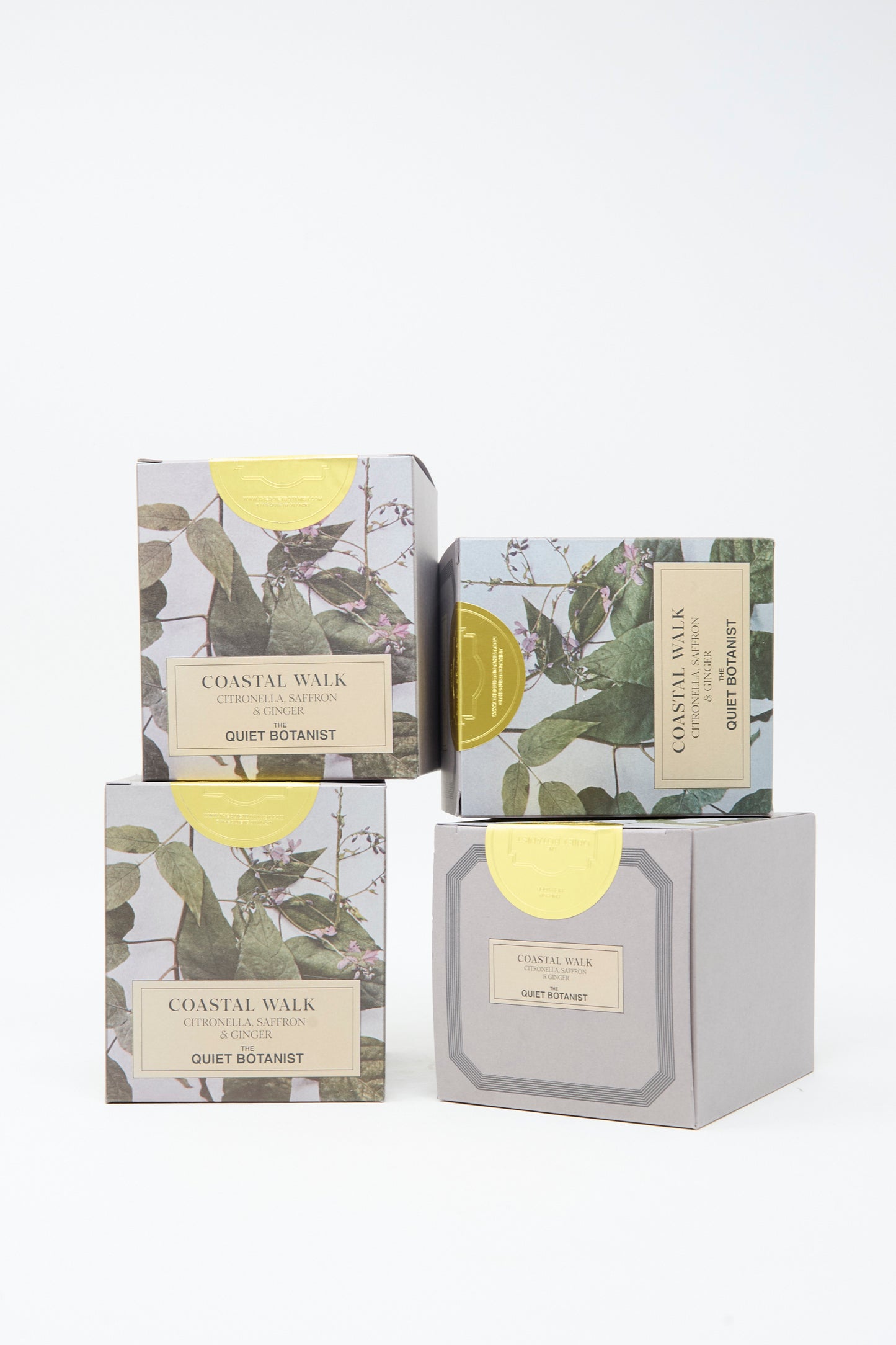Four boxes of The Quiet Botanist soap, adorned with botanical illustrations and labels, are stacked on a white background, evoking the artistry seen in their Limited Edition Summer Candle Coastal Walk collection crafted from natural coconut wax.