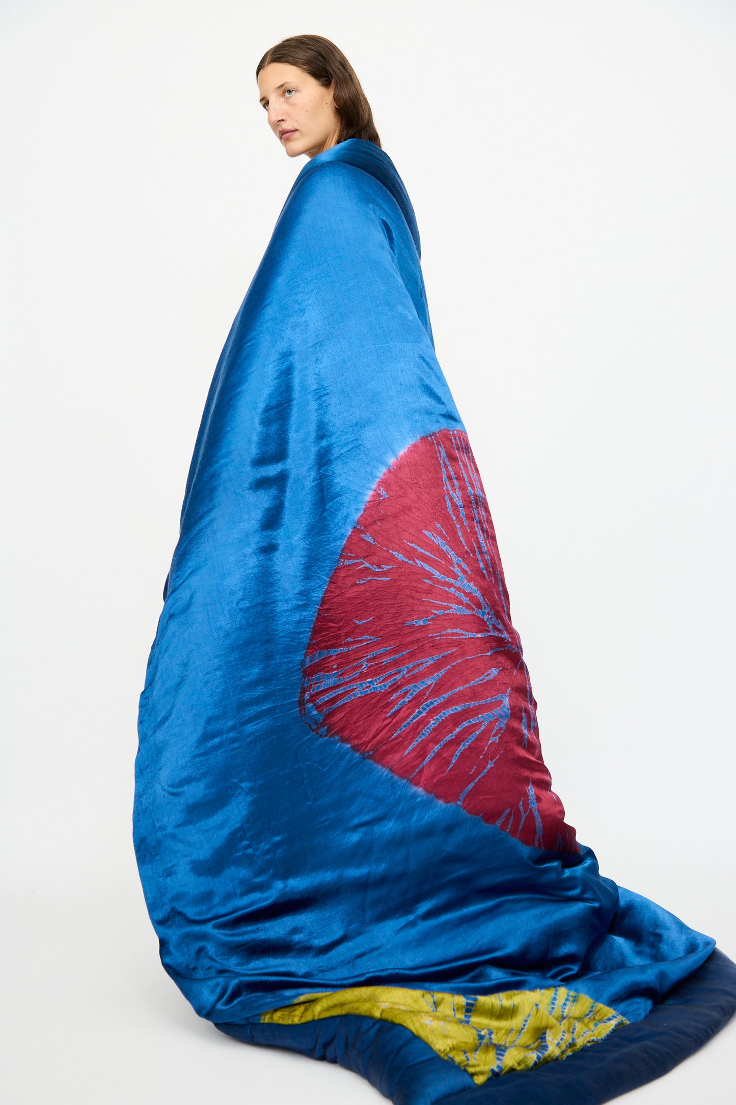 A person stands wrapped in the TIGRA TIGRA Moon Dye Quilt in Jewel Blue, Acid Green, and Magenta, made in India, against a plain white background.