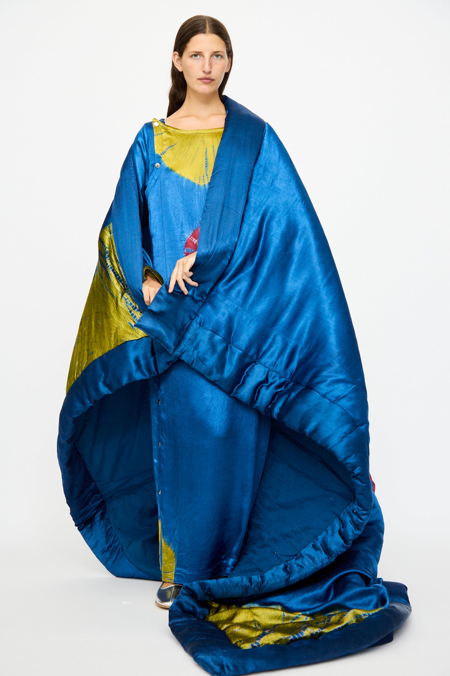 A woman wears TIGRA TIGRA’s Moon Dye Quilt in Jewel Blue and Acid Green—its voluminous, sculptural silk drapes to the floor—posing against a plain white background.