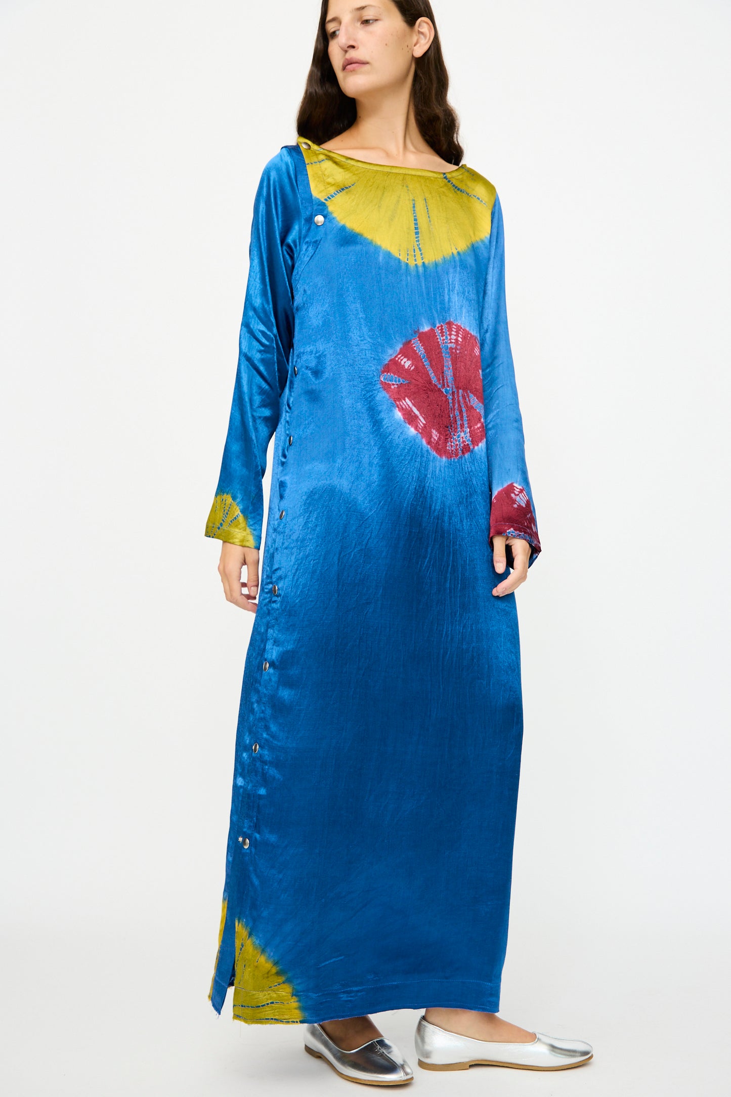 A woman wears the TIGRA TIGRA Shibori Snap Dress in Jewel Blue, Acid Green, and Magenta with silver flats, standing against a plain white background.