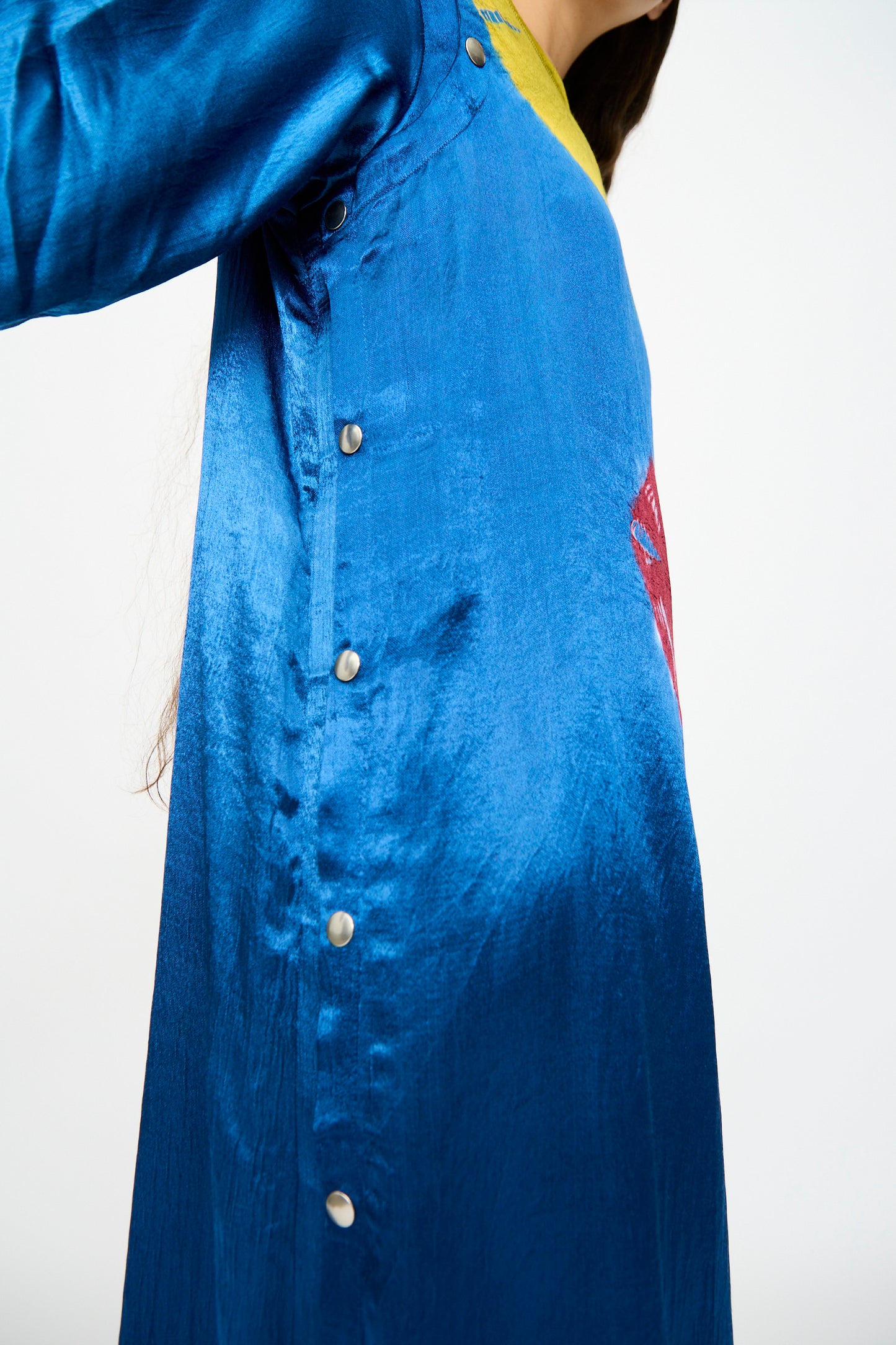 Model wears the TIGRA TIGRA Shibori Snap Dress in Jewel Blue, featuring side buttons, photographed from below with one arm raised against a plain light background.
