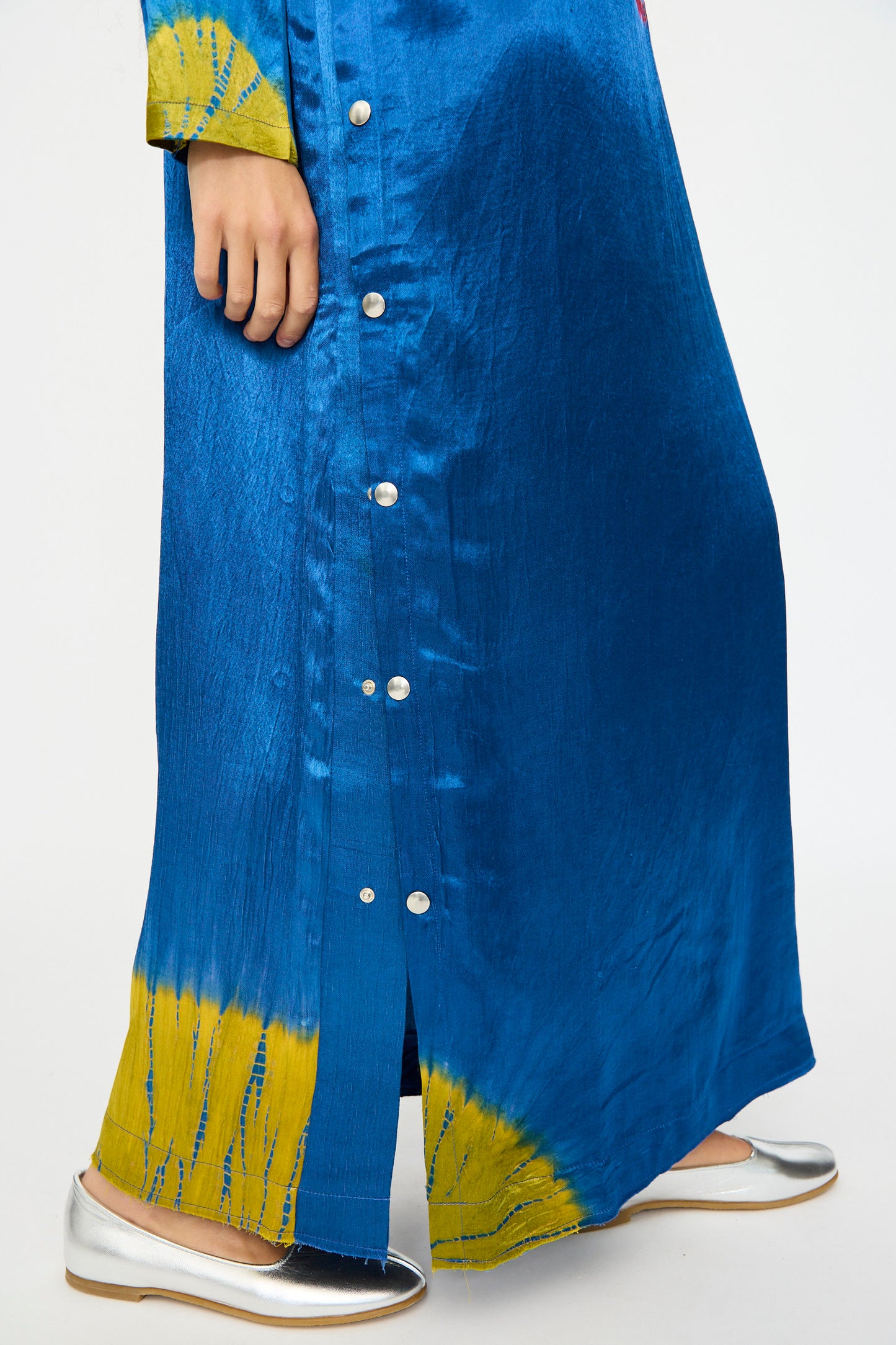 A person wearing the TIGRA TIGRA Shibori Snap Dress in Jewel Blue, Acid Green, and Magenta with silver flat shoes.