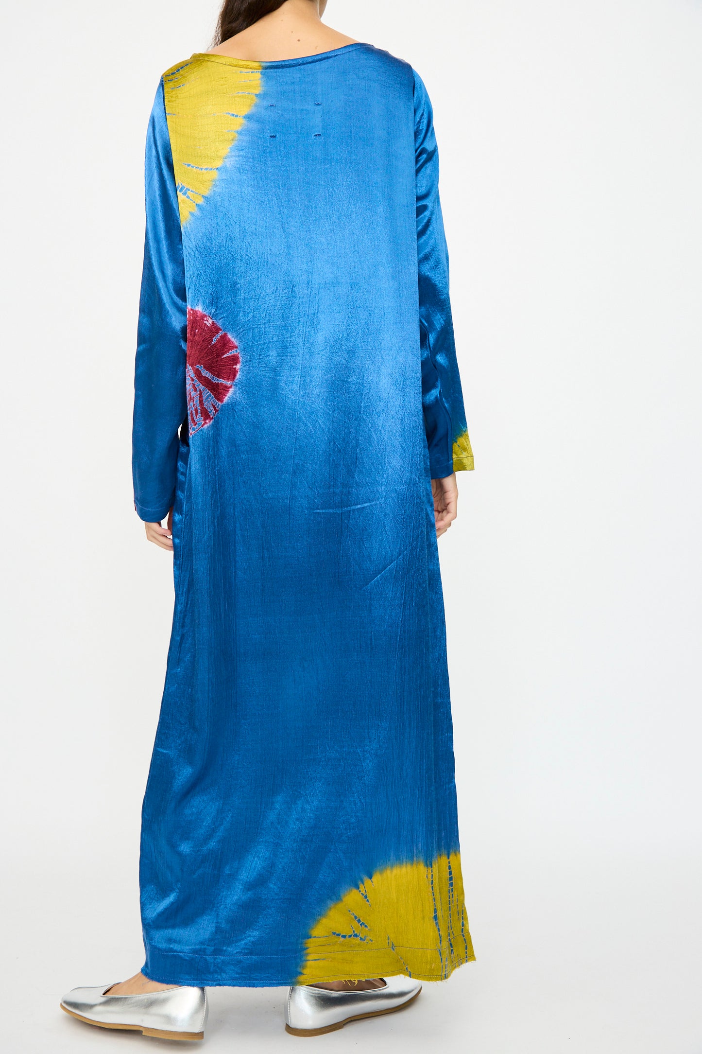 A person seen from the back wears the TIGRA TIGRA Shibori Snap Dress in jewel blue, acid green, and magenta with long sleeves, paired with silver shoes. Made in India.