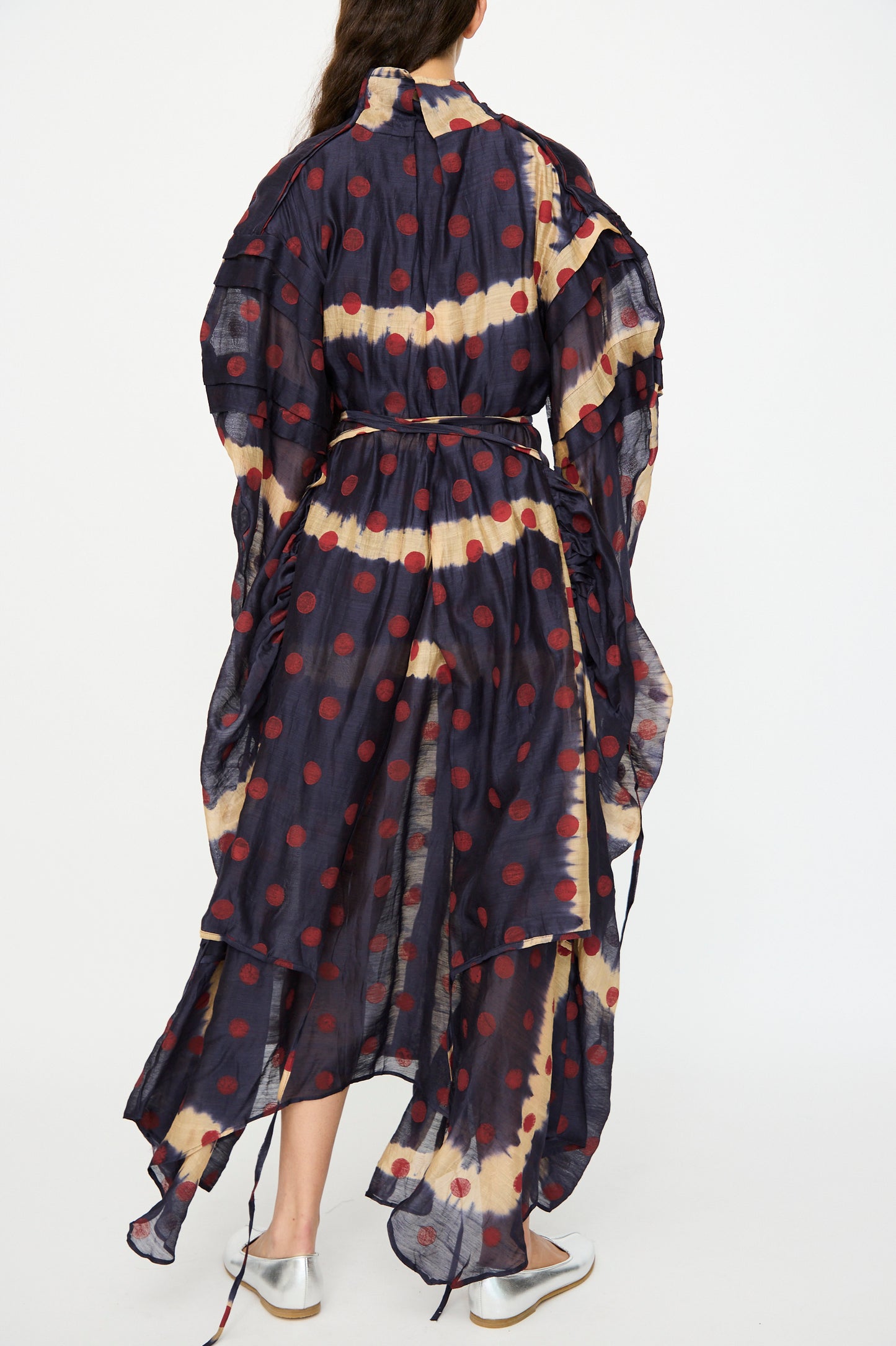A person viewed from the back wears TIGRA TIGRA's Silk Chanderi Teatime Dress in navy, cream, and red. The sheer maxi dress features a belted waist and layered sleeves for an elegant look.
