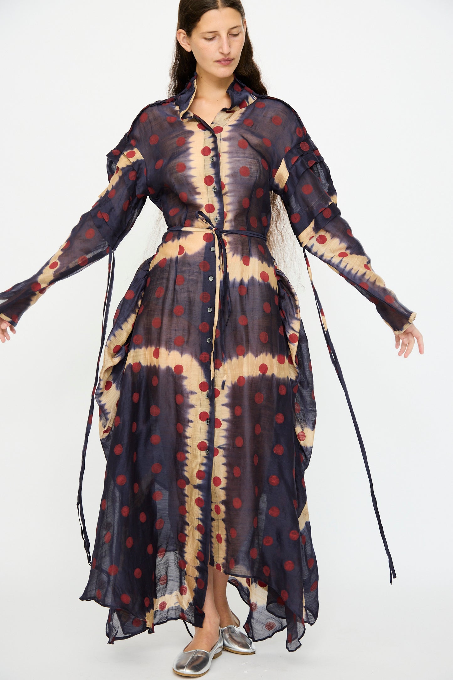 A woman wears the TIGRA TIGRA Silk Chanderi Teatime Dress in navy, cream, and red, featuring loose ties on the sleeves and sides, paired with metallic shoes.