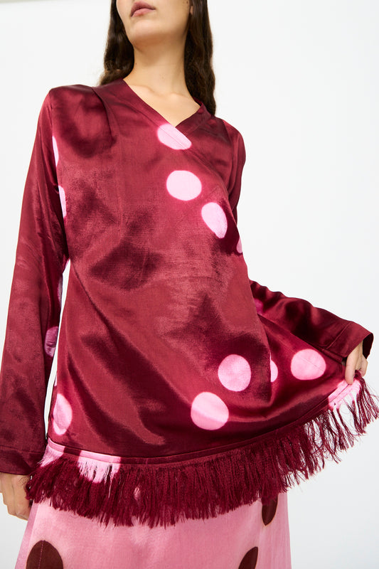 A person wearing the TIGRA TIGRA Silk Mashroo Moon Dye Wrap Top in Maroon, styled with a pink skirt featuring brown dots.