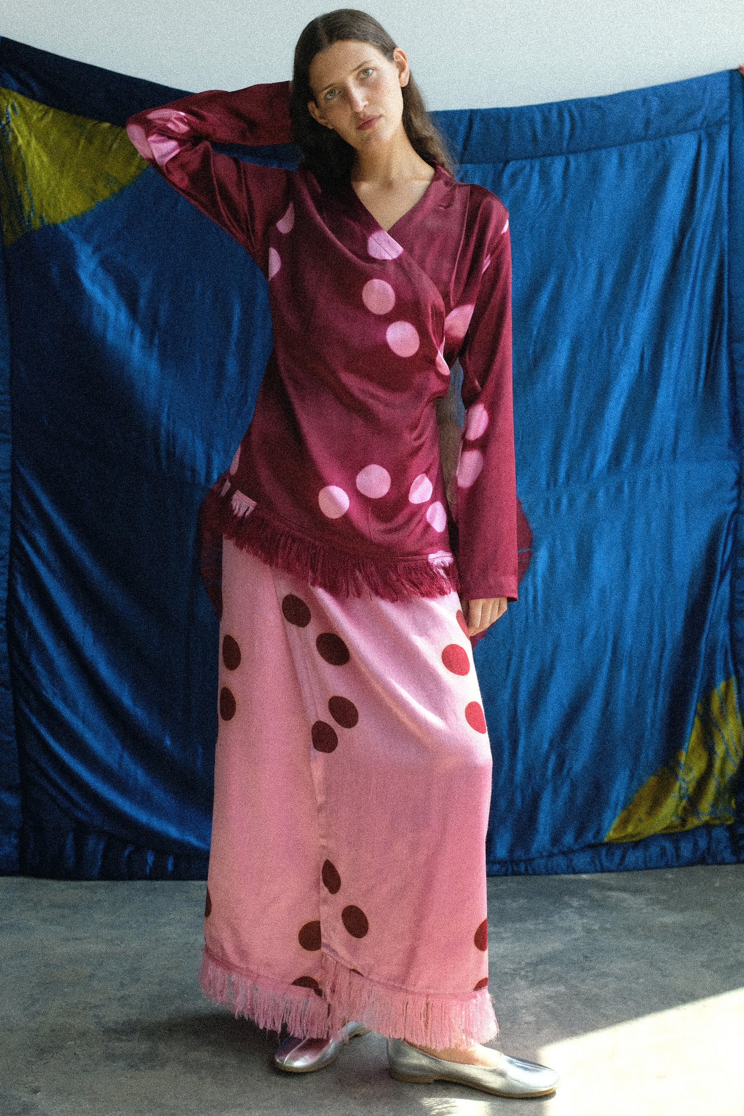 Woman wearing a maroon top with pink polka dots and a pink skirt with red polka dots against a colorful backdrop.