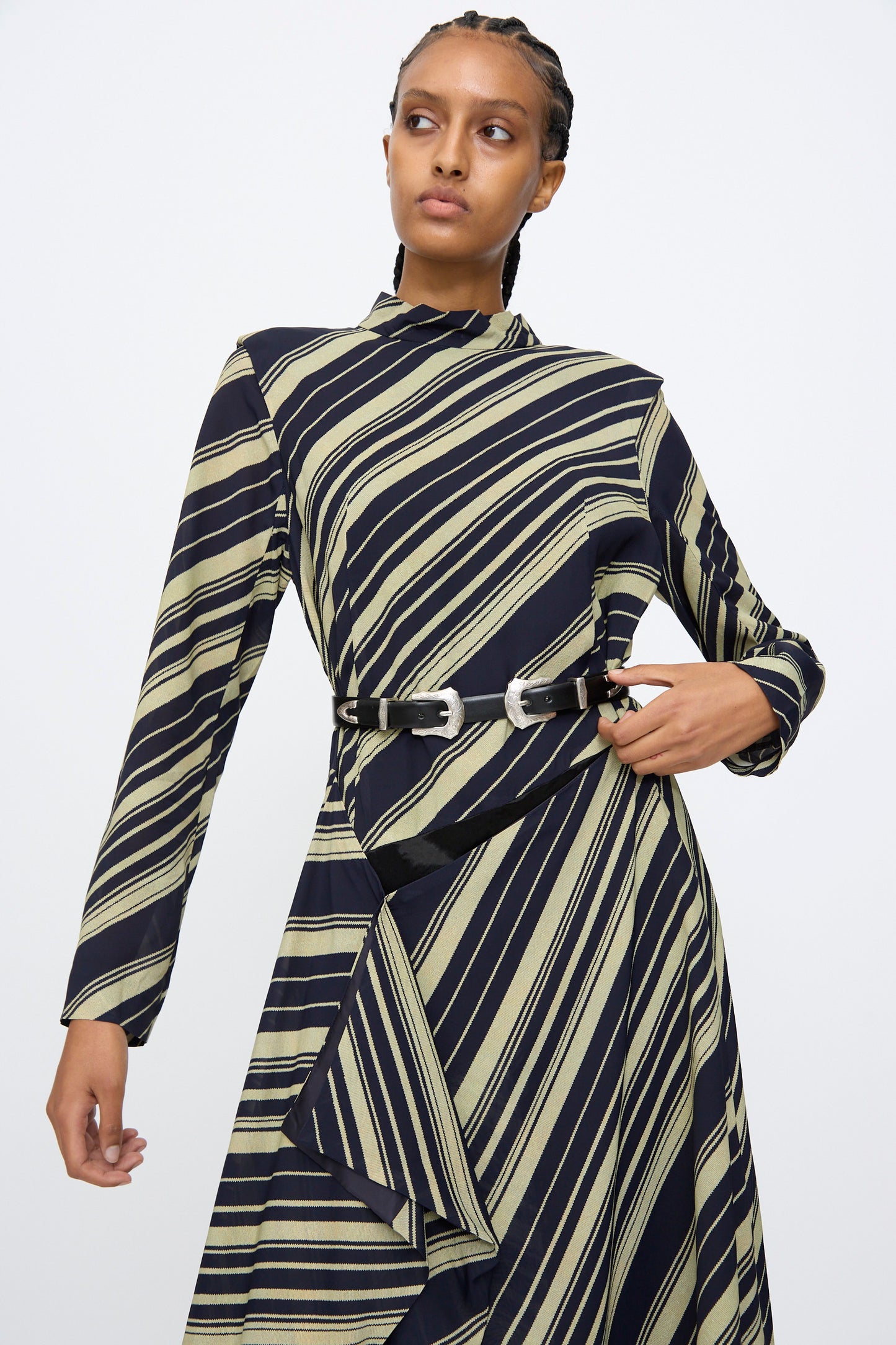 A woman looks to the side against a plain background, wearing a long-sleeved, diagonal-striped dress styled with the TOGA ARCHIVES Double Buckle Belt in Black.