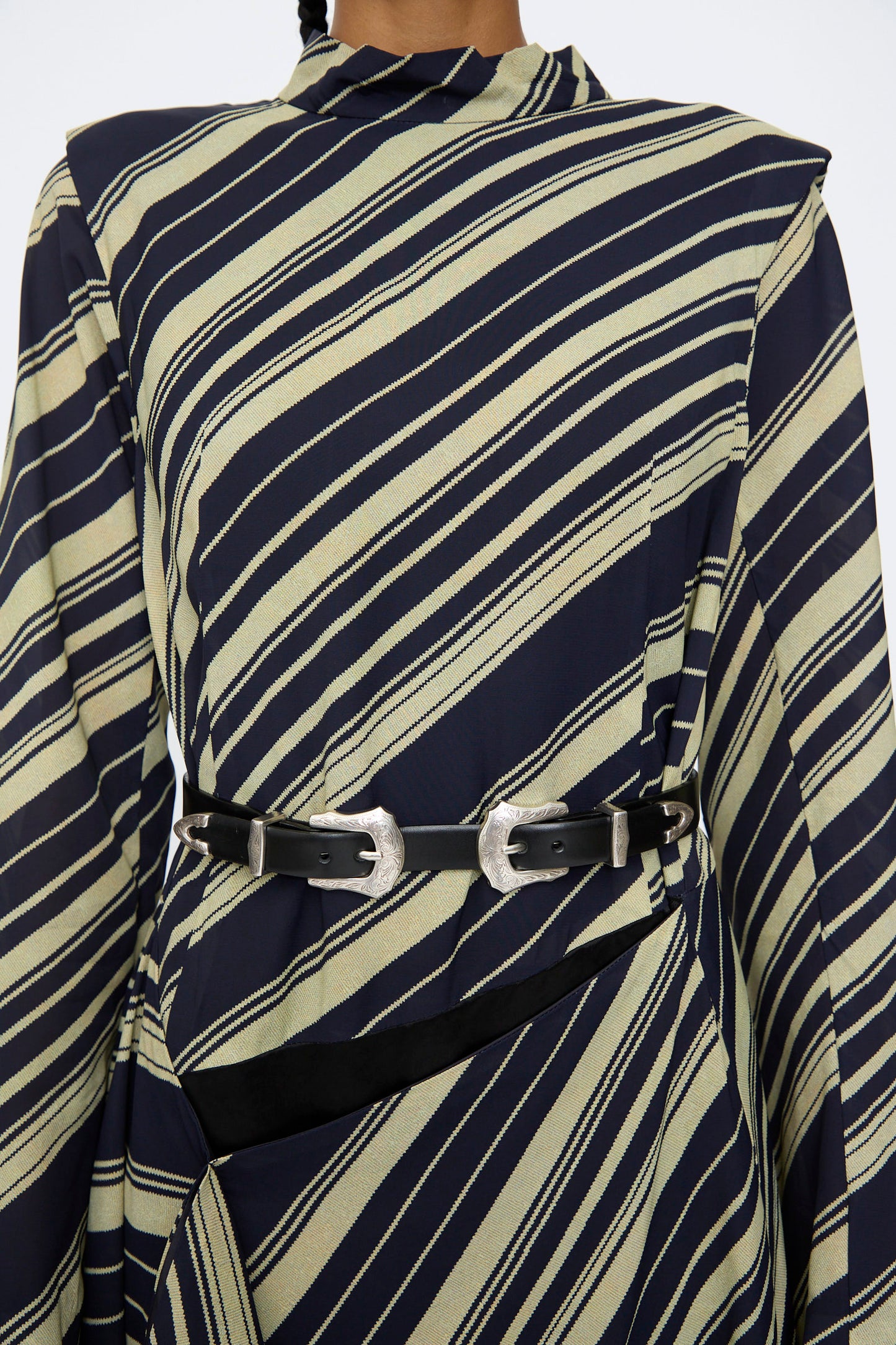 A close-up of a person wearing a navy and beige diagonally striped garment, cinched at the waist with the TOGA ARCHIVES Double Buckle Belt in Black, featuring two silver-tone buckles.