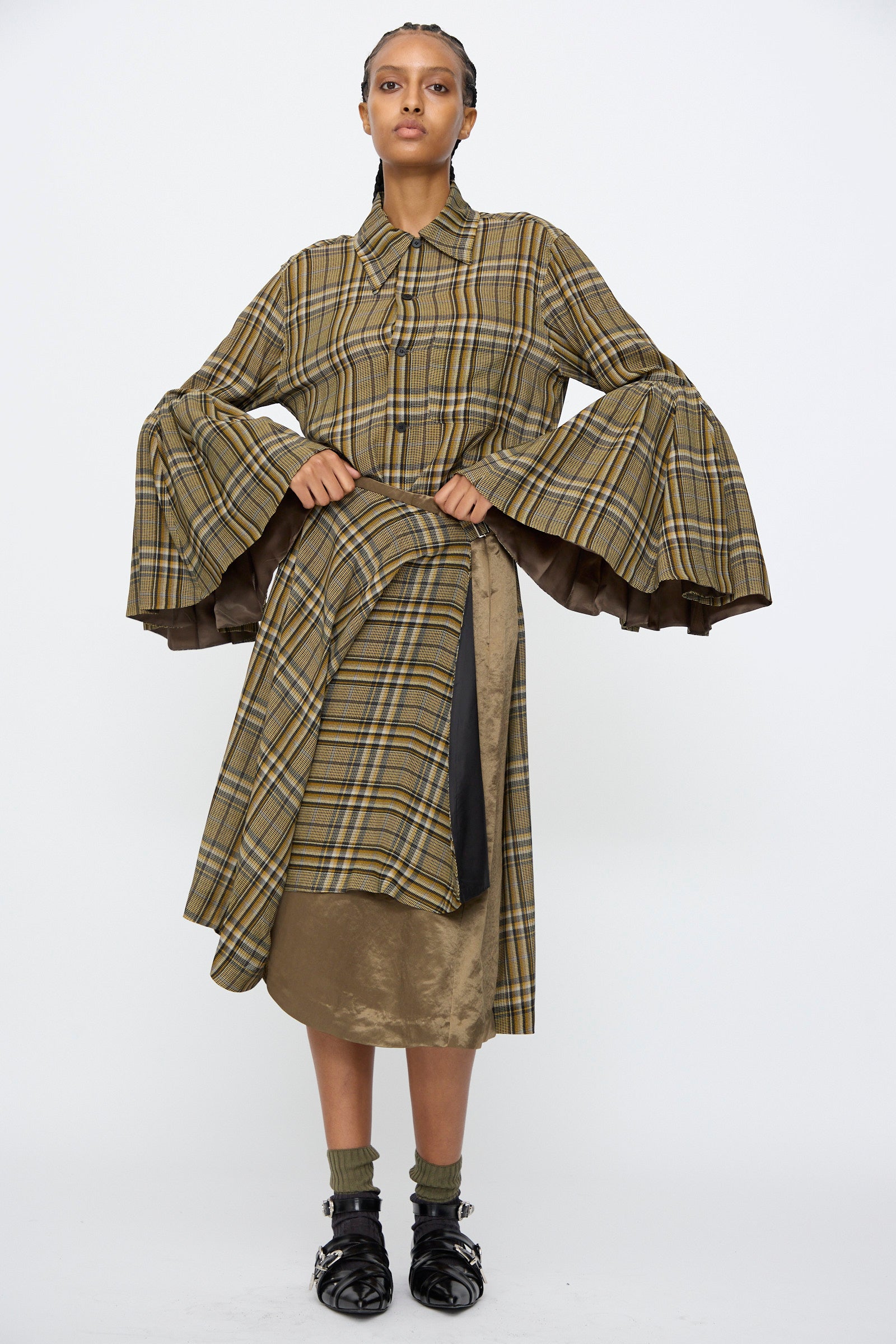A model wears the TOGA ARCHIVES Rayon Print Shirt in Brown, featuring a plaid pattern and wide bell sleeves, styled with an asymmetrical skirt overlay and black shoes with socks. Made in Japan.