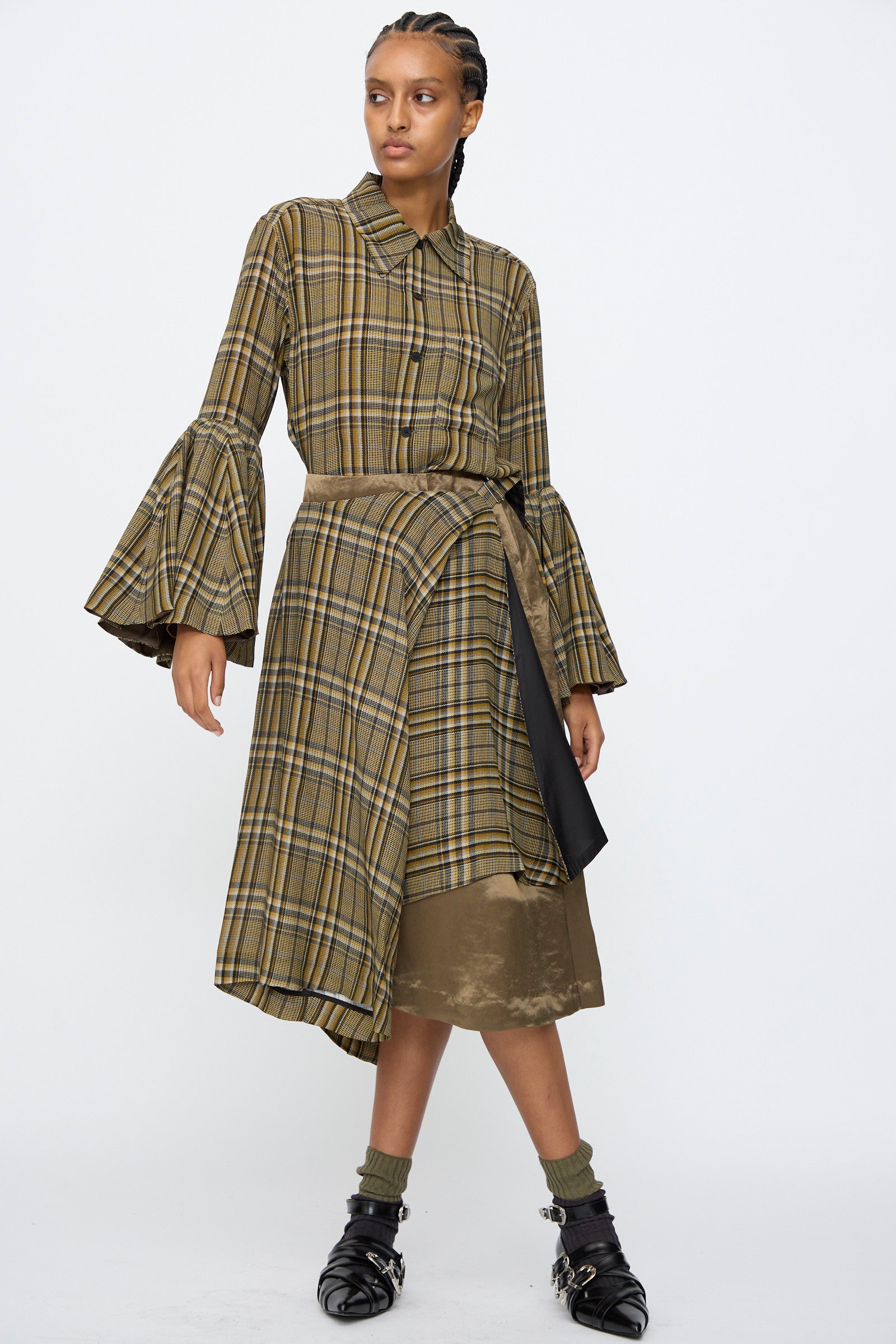 A person wearing the TOGA ARCHIVES Rayon Print Skirt in Brown, paired with flared sleeves, green socks, and black buckled shoes, stands against a plain white background.