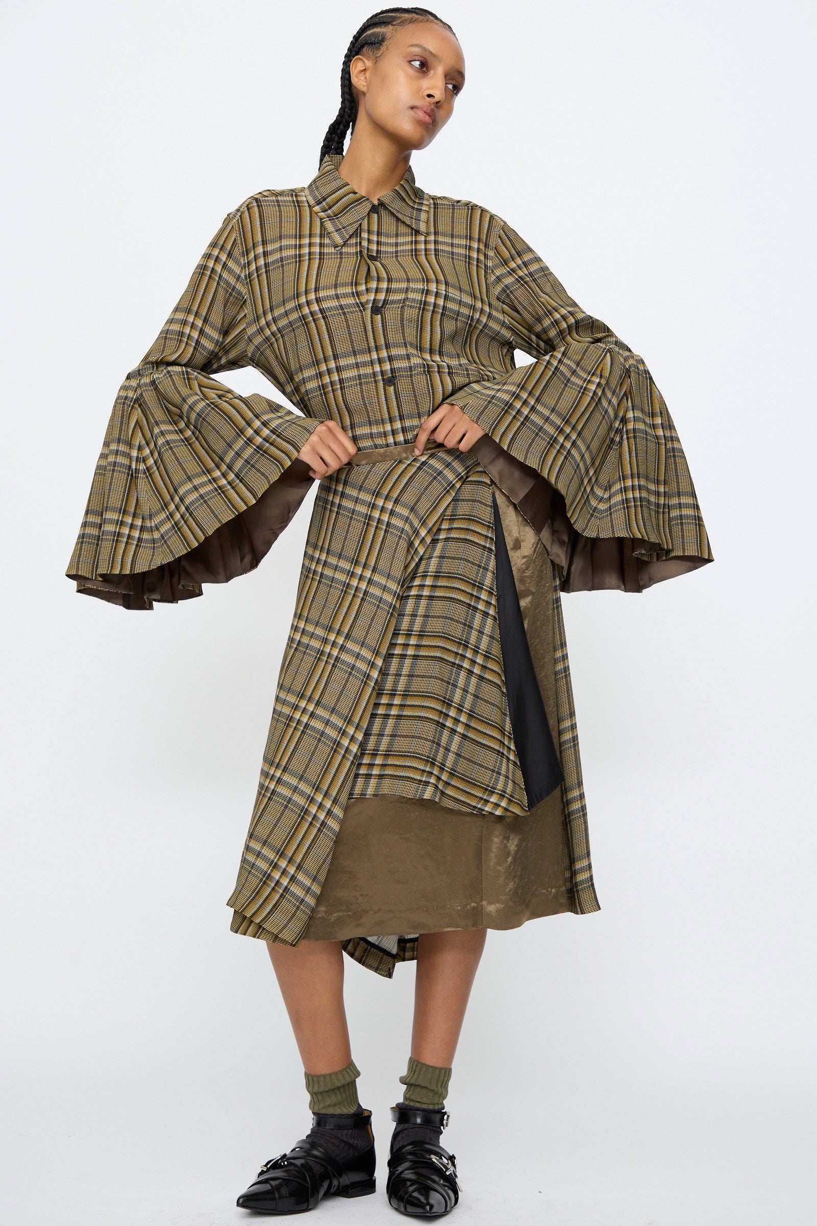 Model wearing TOGA ARCHIVES Rayon Print Skirt in Brown with a plaid top featuring flared sleeves, styled against a plain white background.