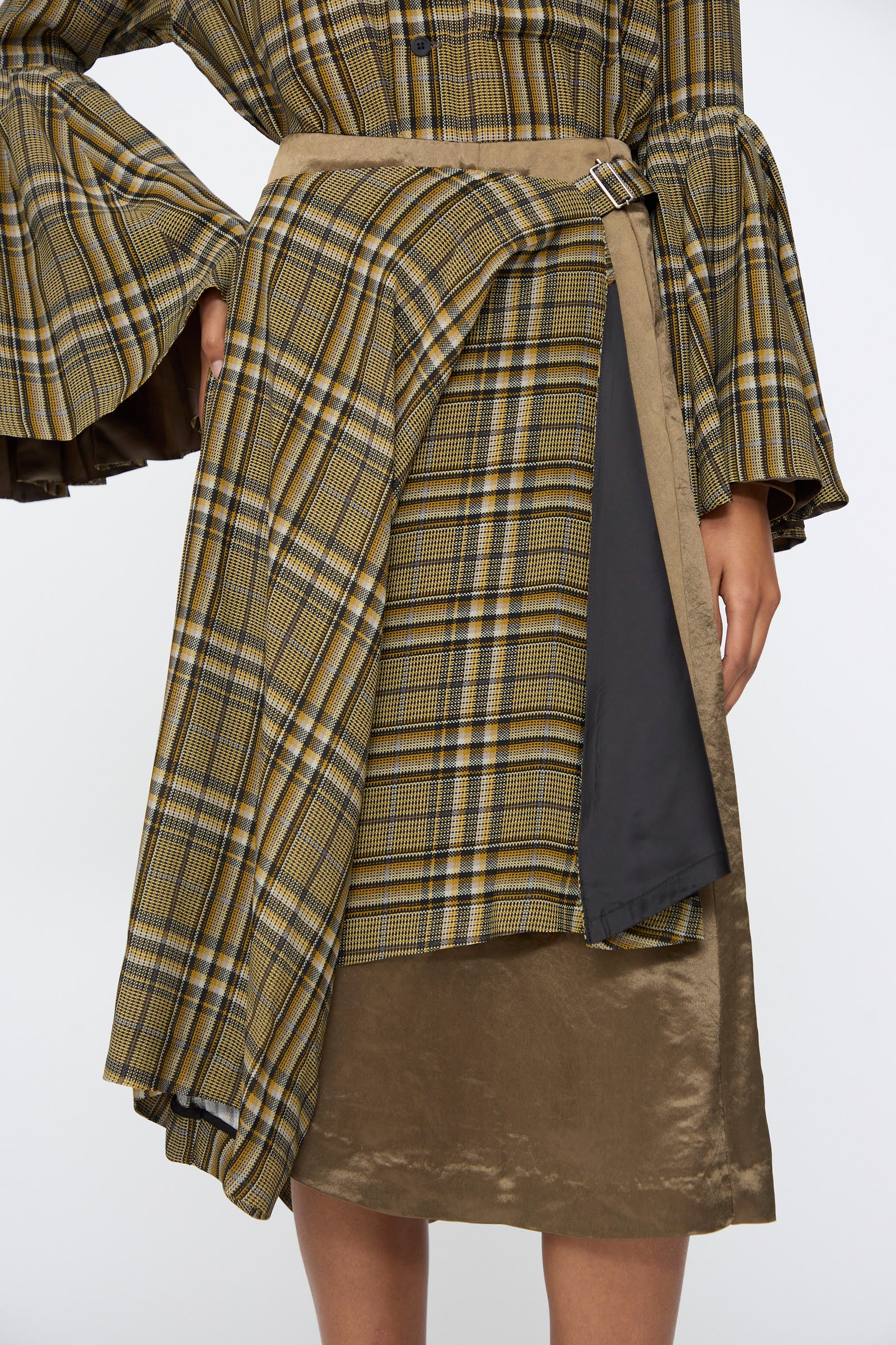 A person wears the TOGA ARCHIVES Rayon Print Skirt in Brown, styled as an asymmetrical midi with layered fabric and a metal buckle, paired with a matching plaid top featuring flared sleeves.