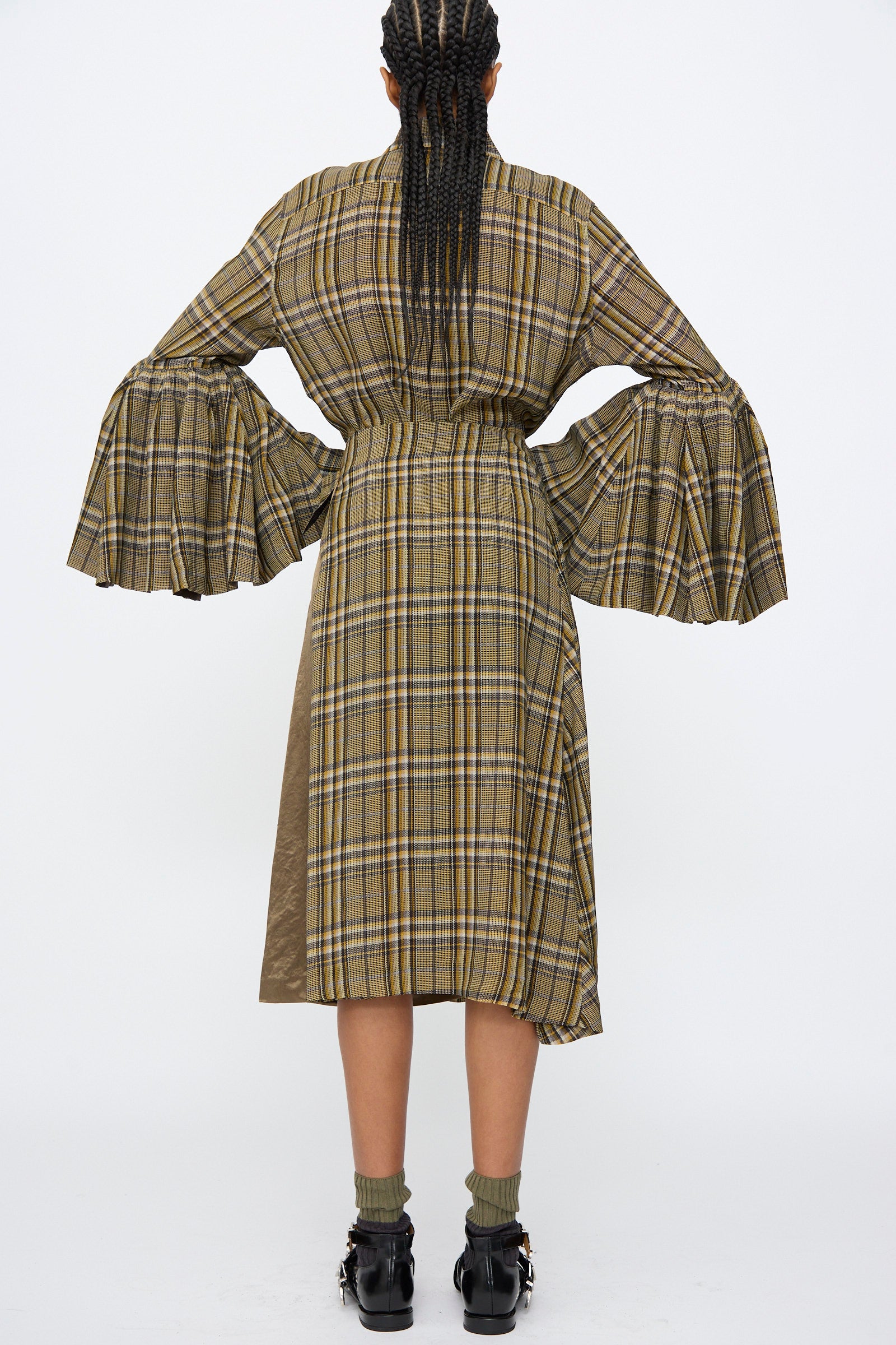 A person with braided hair wears the TOGA ARCHIVES Rayon Print Skirt in Brown, paired with wide bell sleeves, green socks, and black shoes.