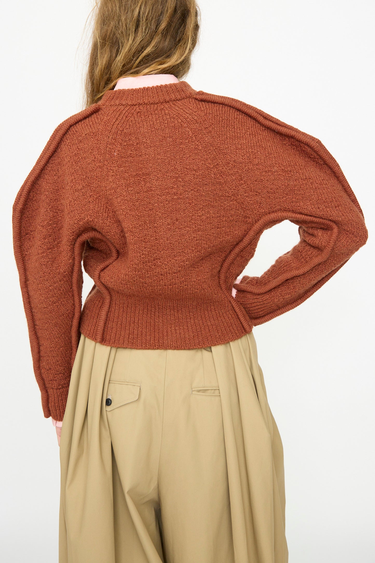 A person stands with their back to the camera, wearing the TOGA ARCHIVES Motif Knit Cardigan in Brown and beige pleated pants against a plain white background.