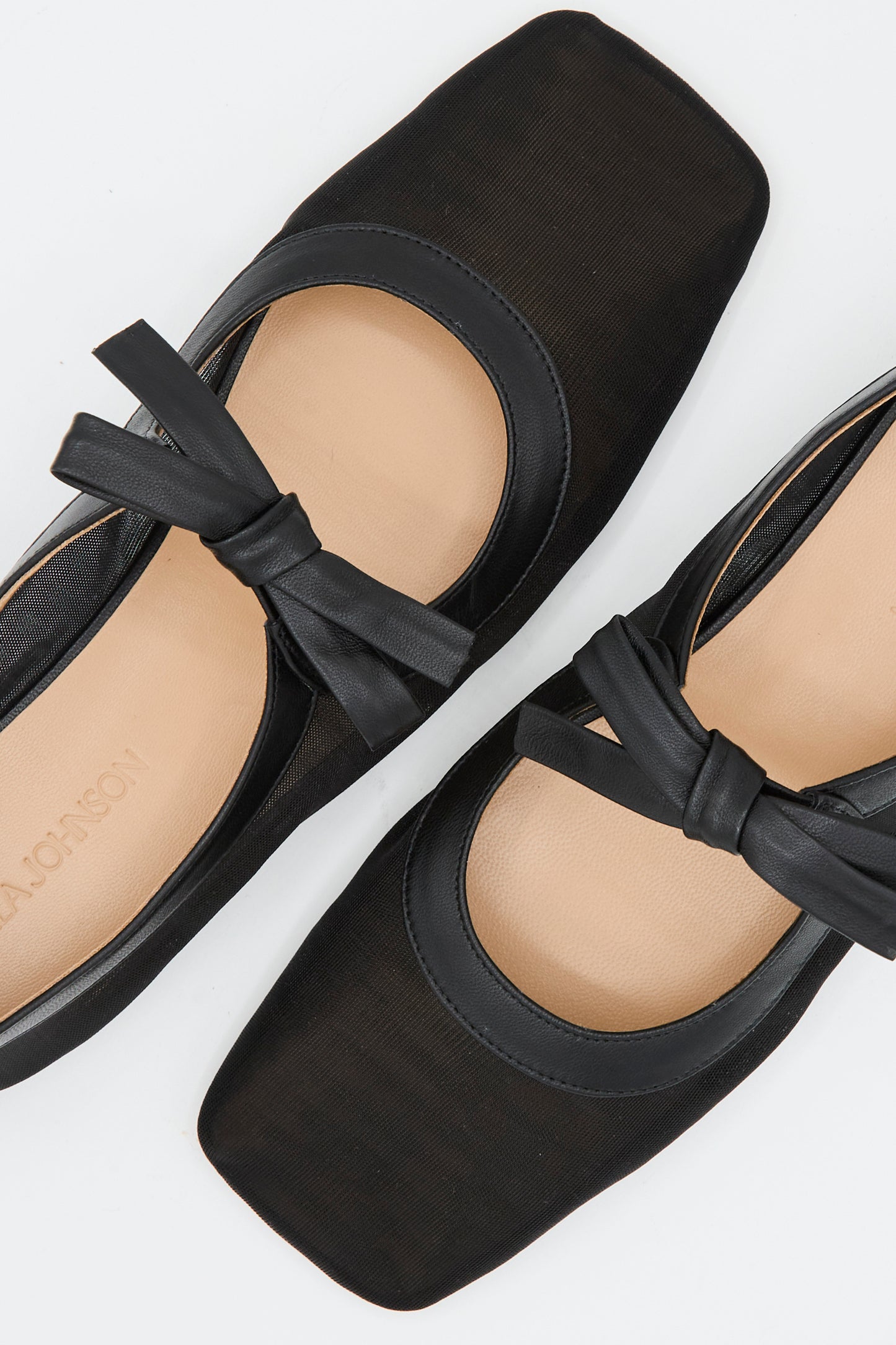 The Ulla Johnson Cleo Flat in Noir is a pair of black napa leather square-toe ballet flats with front bow details, made in Italy and shown from above on a white background.