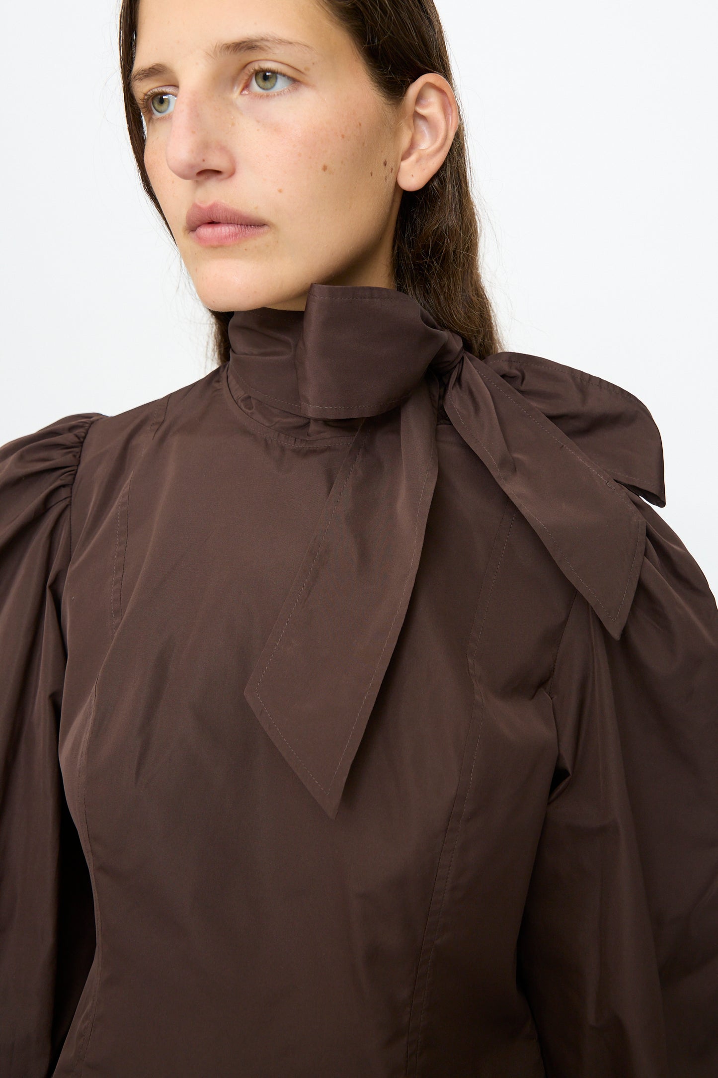 A person wears the Ulla Johnson Giorgia Silk Blouse in Sequoia, featuring a large bow neck and balloon sleeves, standing against a plain white background.