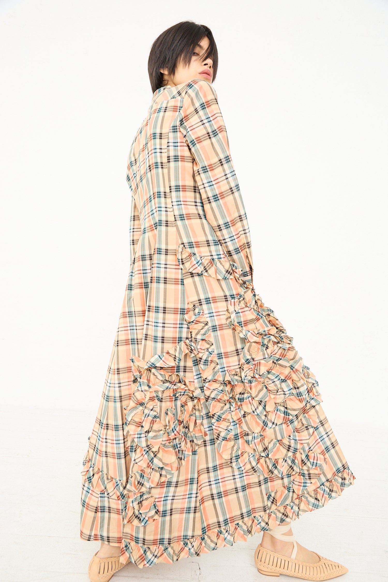 Woman wearing a long plaid maxi shirt dress with ruffle detailing, looking over her shoulder. (Gwen Dress in Meadow by Ulla Johnson)