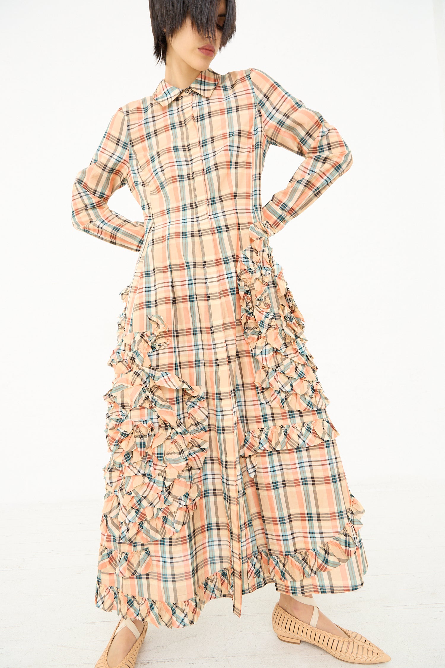 A person modeling an Ulla Johnson Gwen Dress in Meadow, a long-sleeved, plaid maxi shirt dress with ruffle detailing, paired with beige pointed shoes.