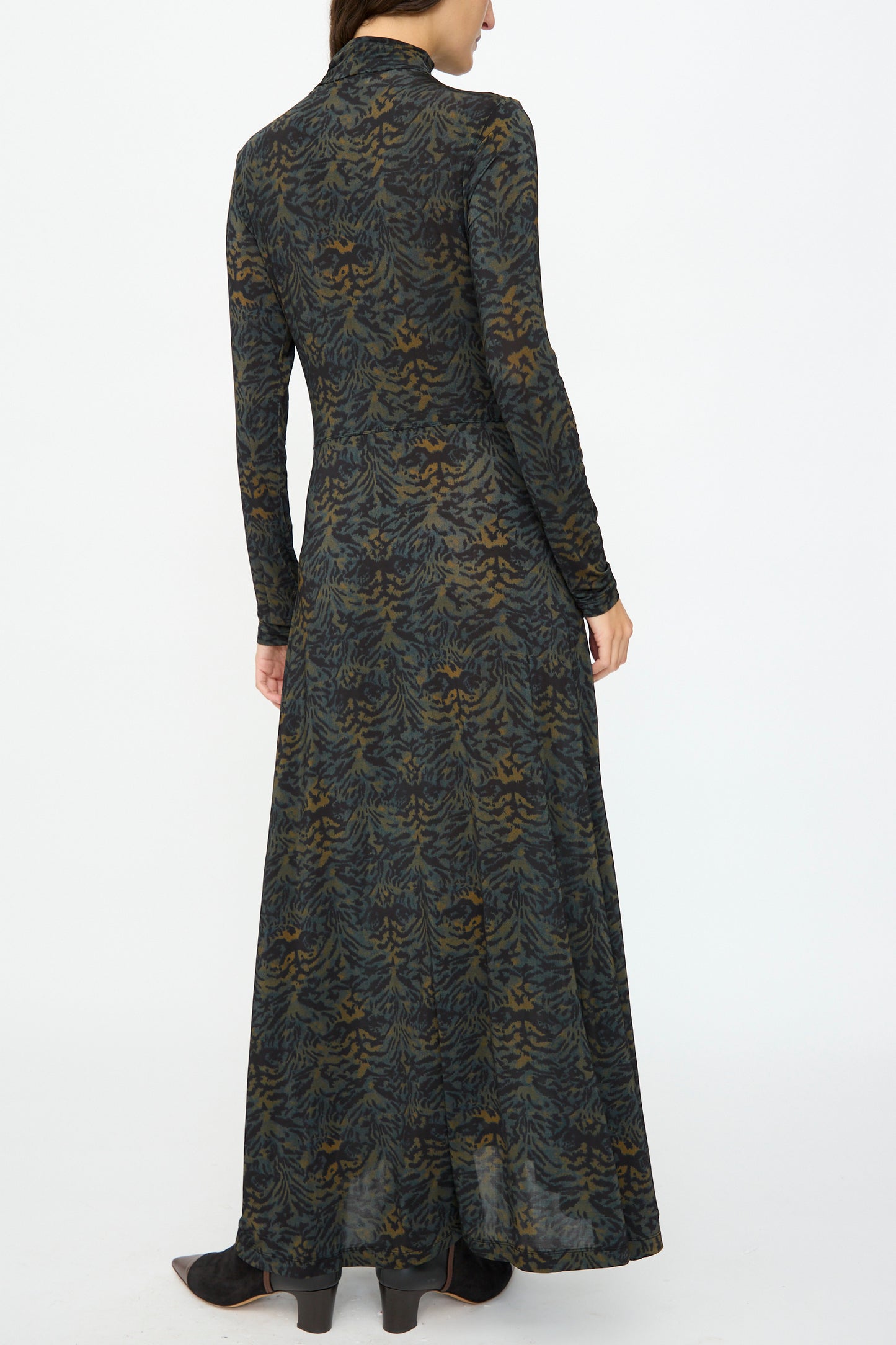 A person faces away from the camera on a plain white background, wearing the Ulla Johnson Koa Dress in Desert Jasper—a slim fit maxi dress with an ikat animal print.