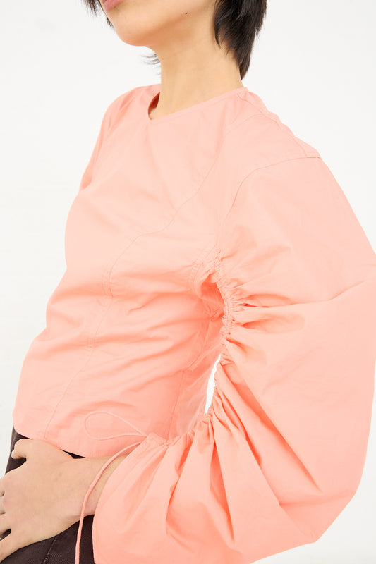 Woman wearing a pink cotton poplin Lorna Blouse in Peony with a gathered detail on the side from Ulla Johnson.