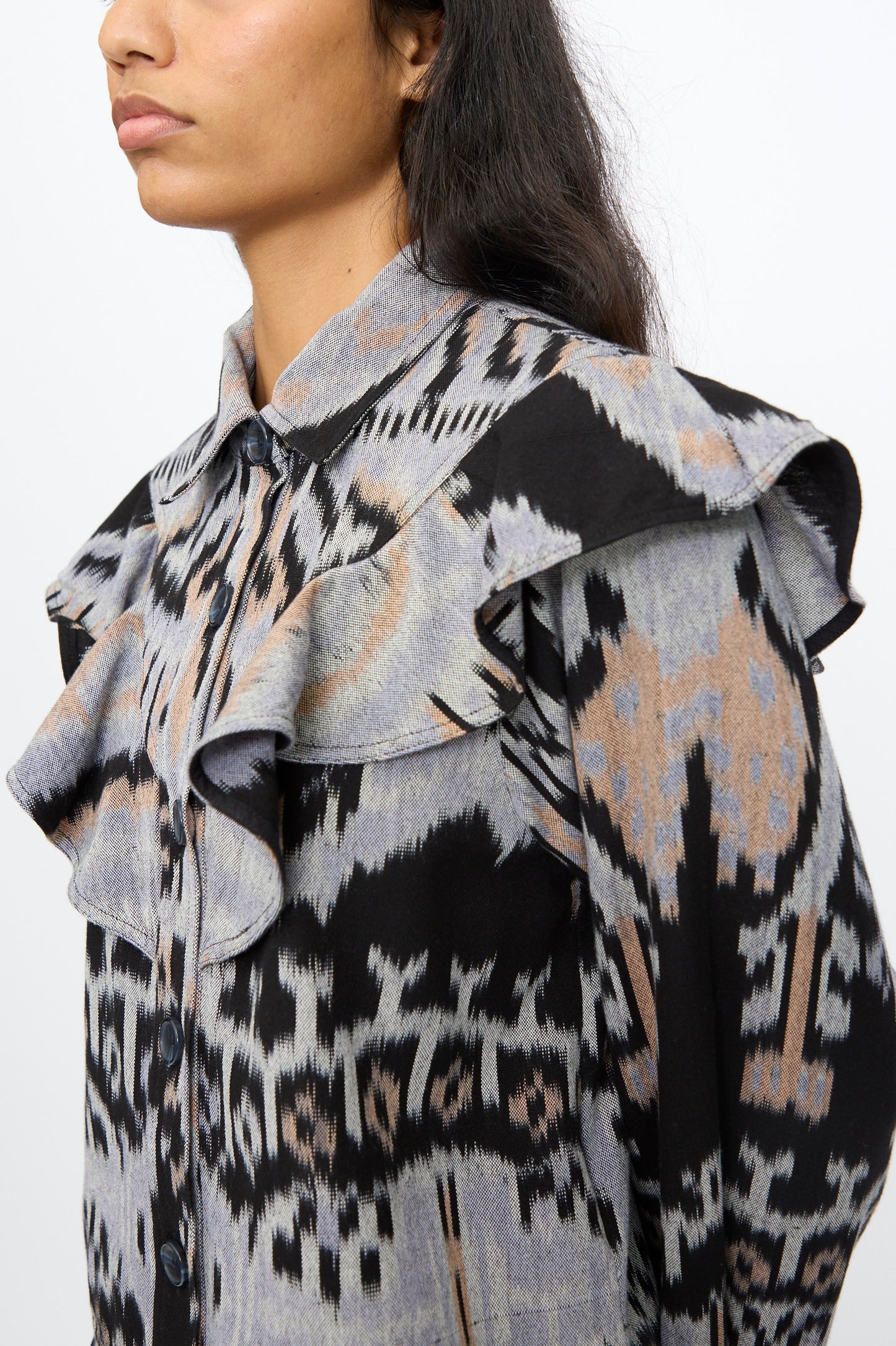 A person wears the Ulla Johnson Mathilde Blouse in Tigereye, a hand-loomed cotton top with chest and shoulder ruffles and an Ikat motif; their face is partially out of frame.