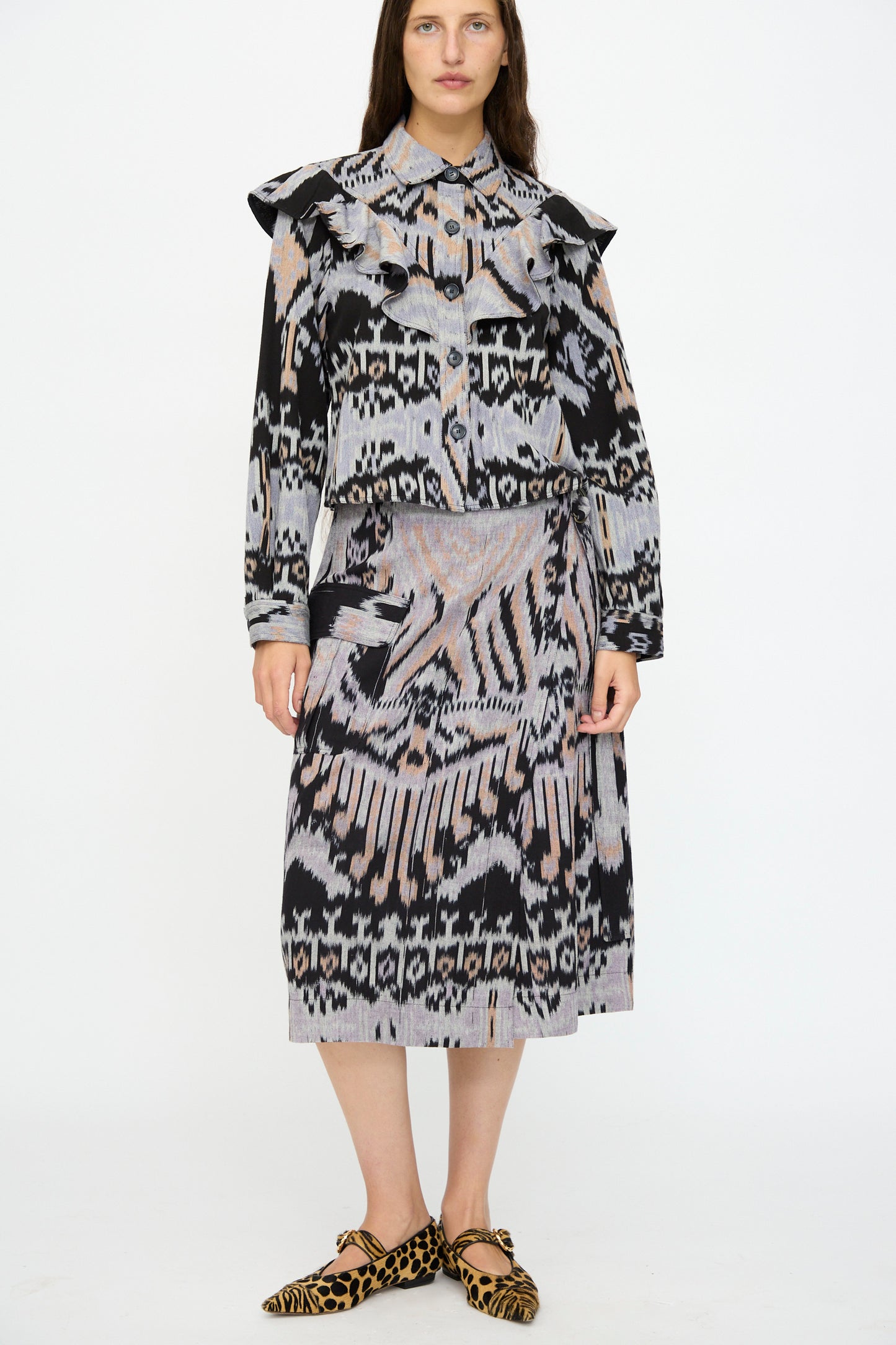 A woman wears a patterned blouse, the Ulla Johnson Mila Pencil Skirt in Tigereye, and leopard-print pointed flats against a plain white background.