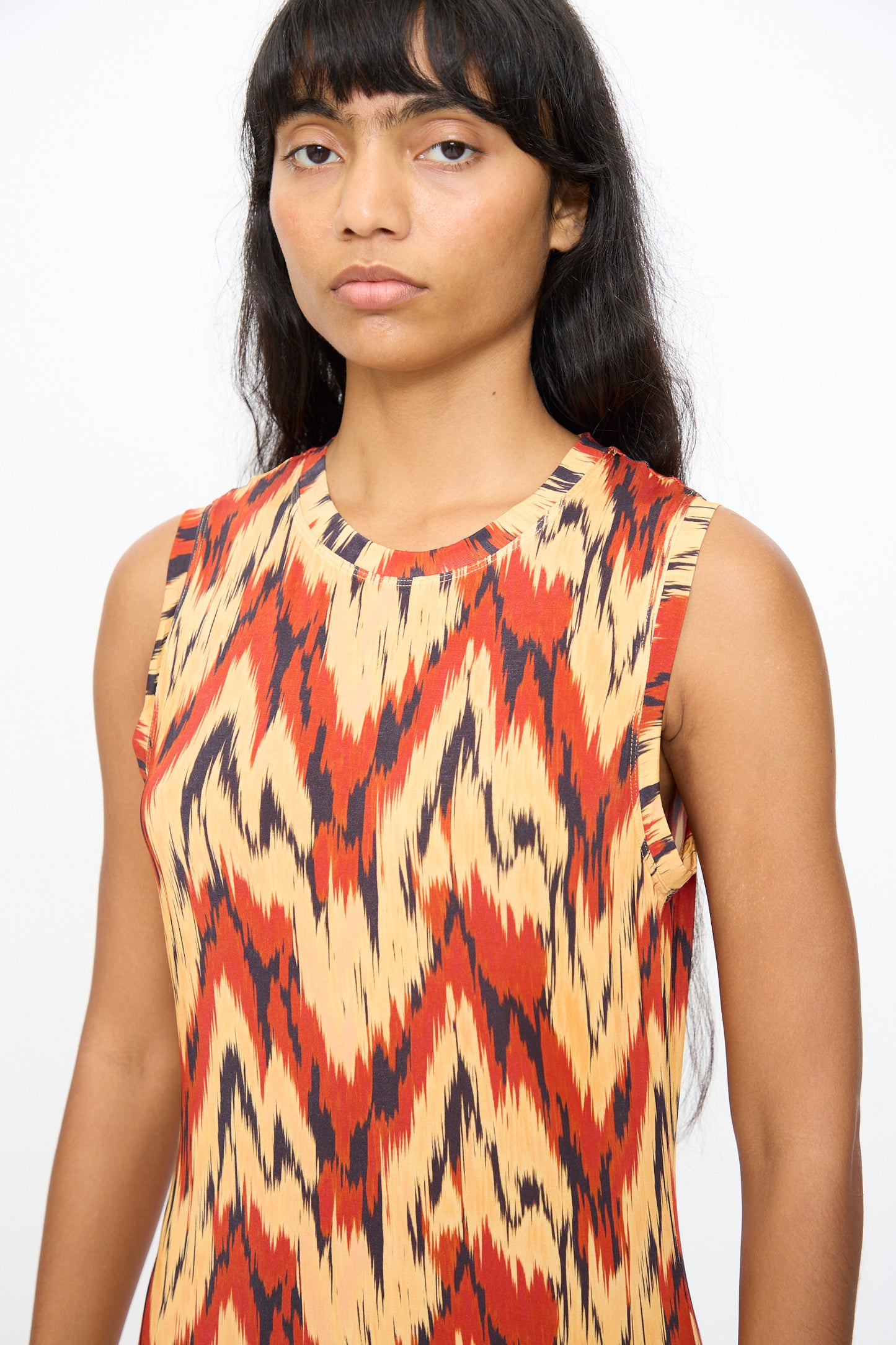 A woman with long dark hair wears the Ulla Johnson Orla Dress in Carnelian, featuring a bold zigzag pattern, standing against a plain white background.