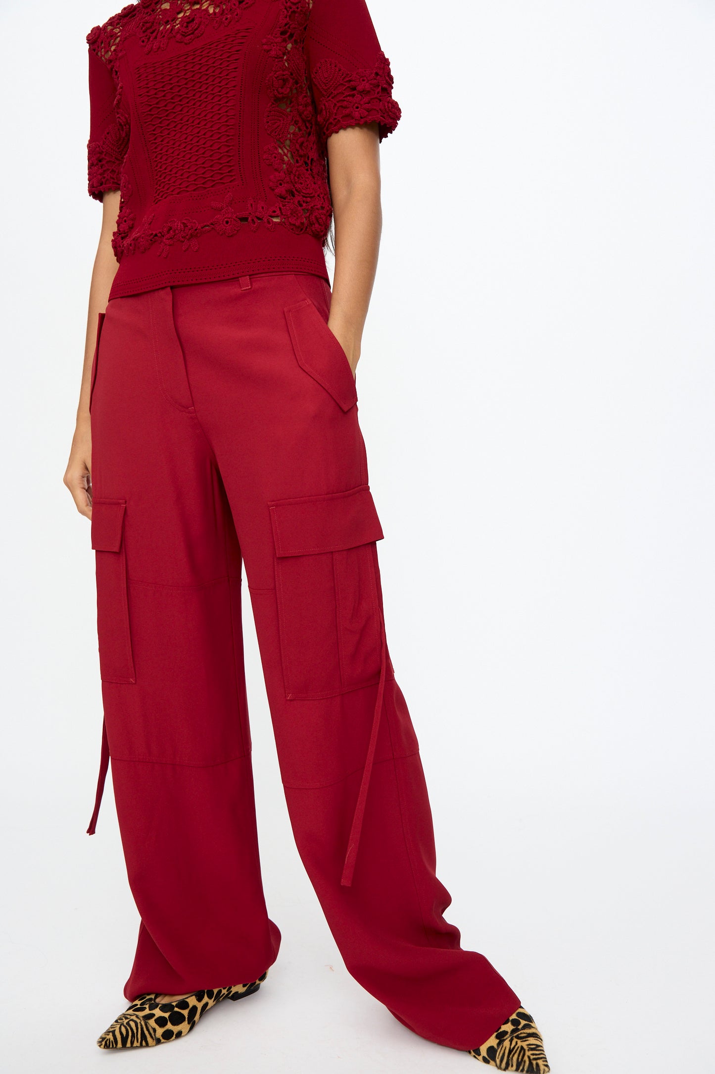 A person wears Ulla Johnson's Pax Pant in Dahlia with a red relaxed fit short-sleeve textured top and leopard print pointed shoes, set against a plain white background.