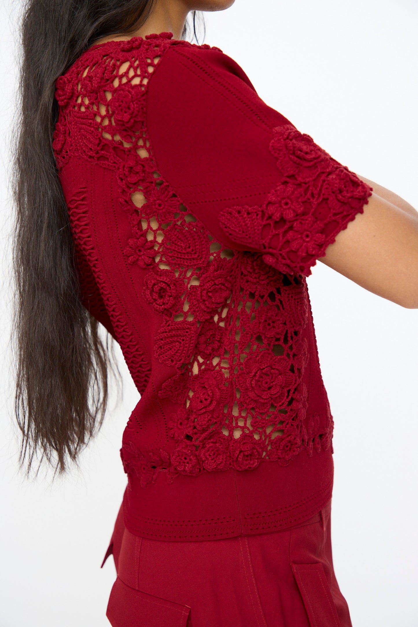 A person wearing the Ulla Johnson Stella Knit Top in Begonia, a short sleeve floral knit top with a scalloped hem, paired with matching red pants and shown from the side.