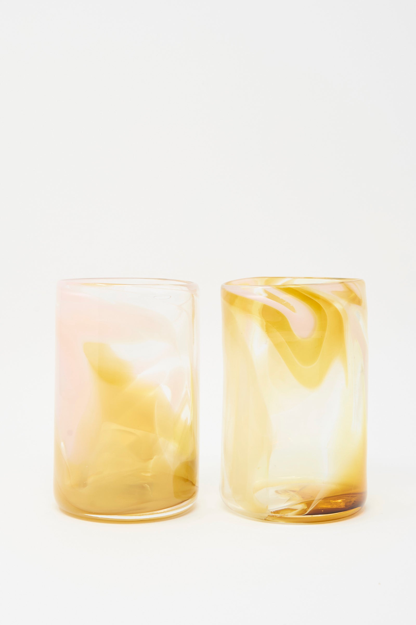 The Upstate Hand Dyed Frankie Glass set includes two hand blown, cylindrical tumblers from NYC, each featuring abstract marbled yellow and pink patterns on white.