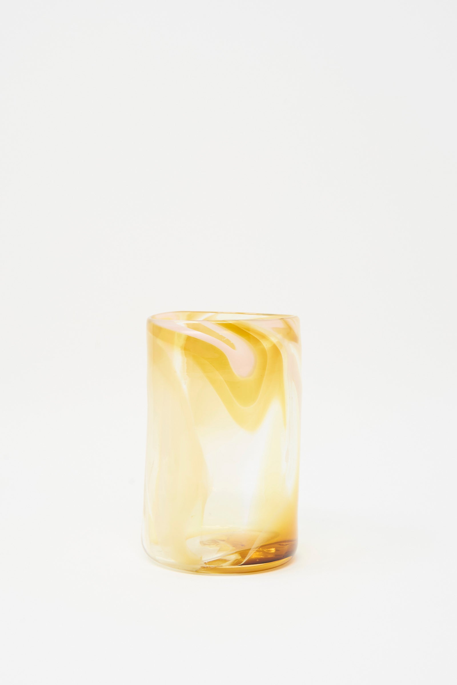 The Hand Dyed Frankie Glass by Upstate is a translucent, cylindrical tumbler featuring abstract amber and yellow swirls, displayed against a plain white background.